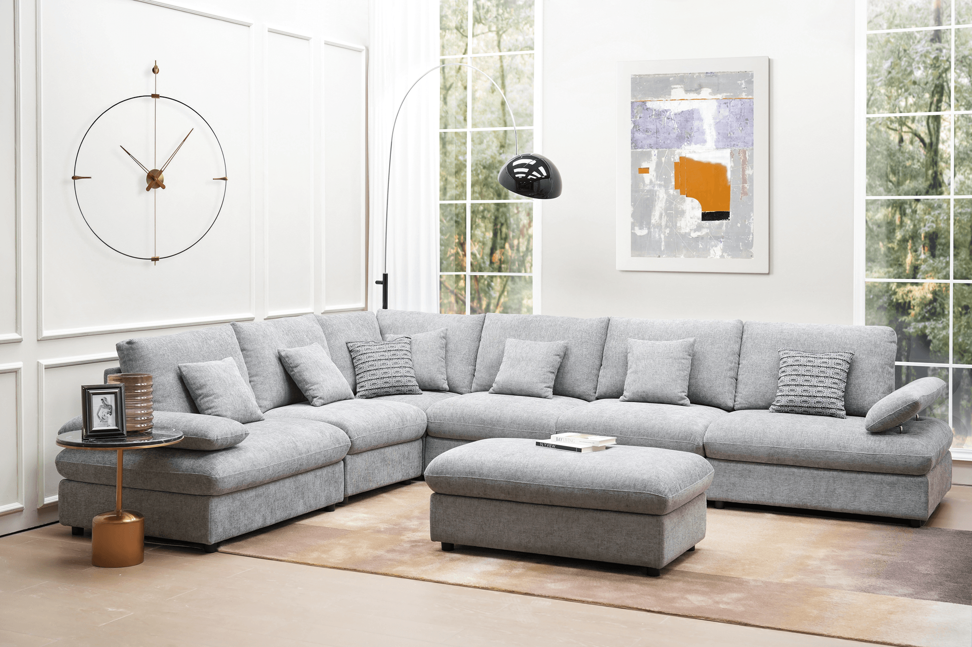 Modern grey sectional sofa with matching ottoman in a bright living room, wall art, and large clock.