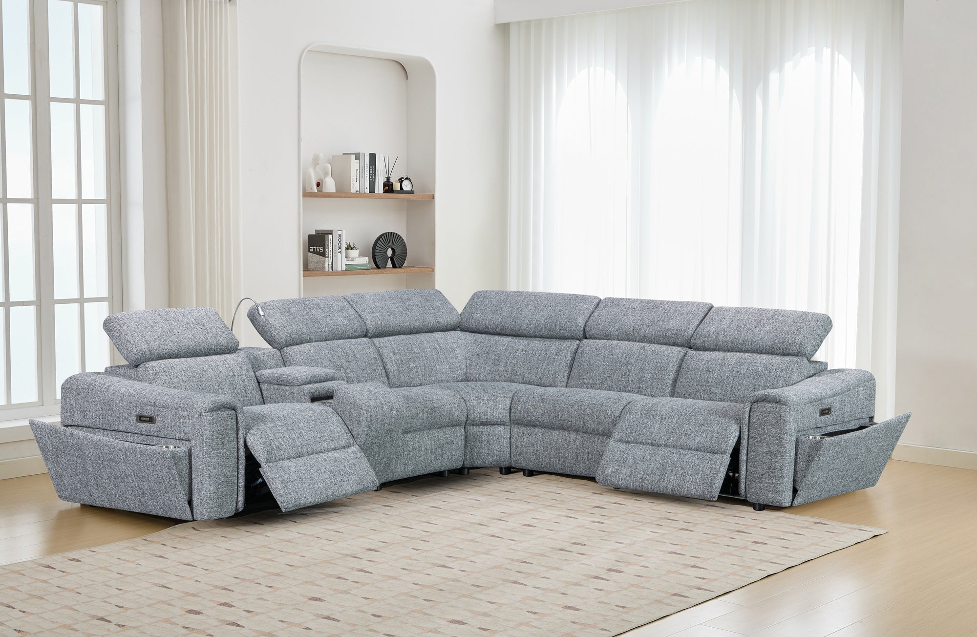 Gray sectional sofa in a living room setting with large windows and a shelf.