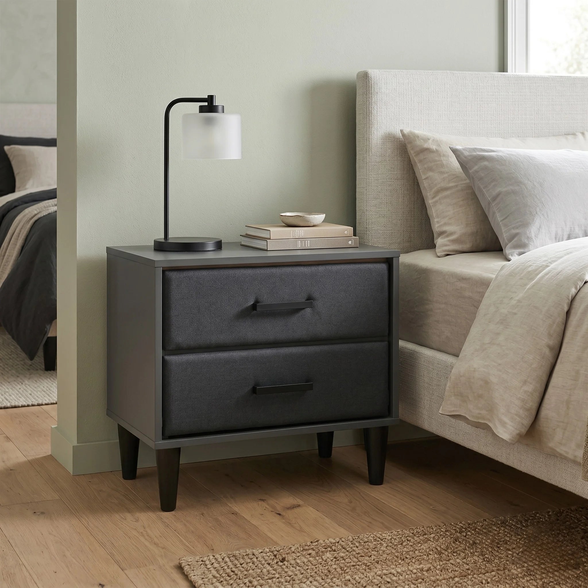 Gray nightstand with two drawers next to a bed in a bedroom setting.