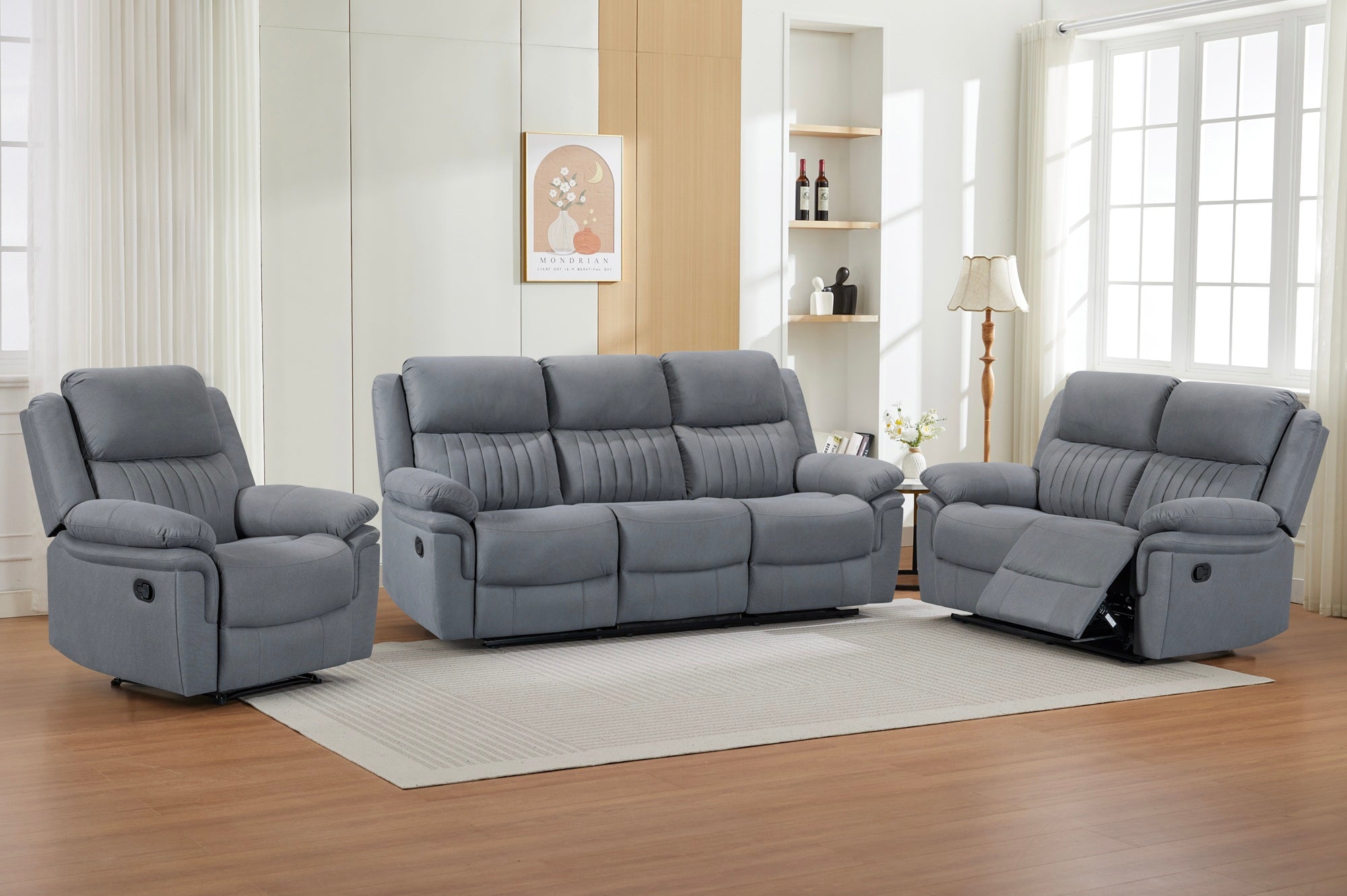 Gray reclining sofa set in a living room with wooden floor and large windows.