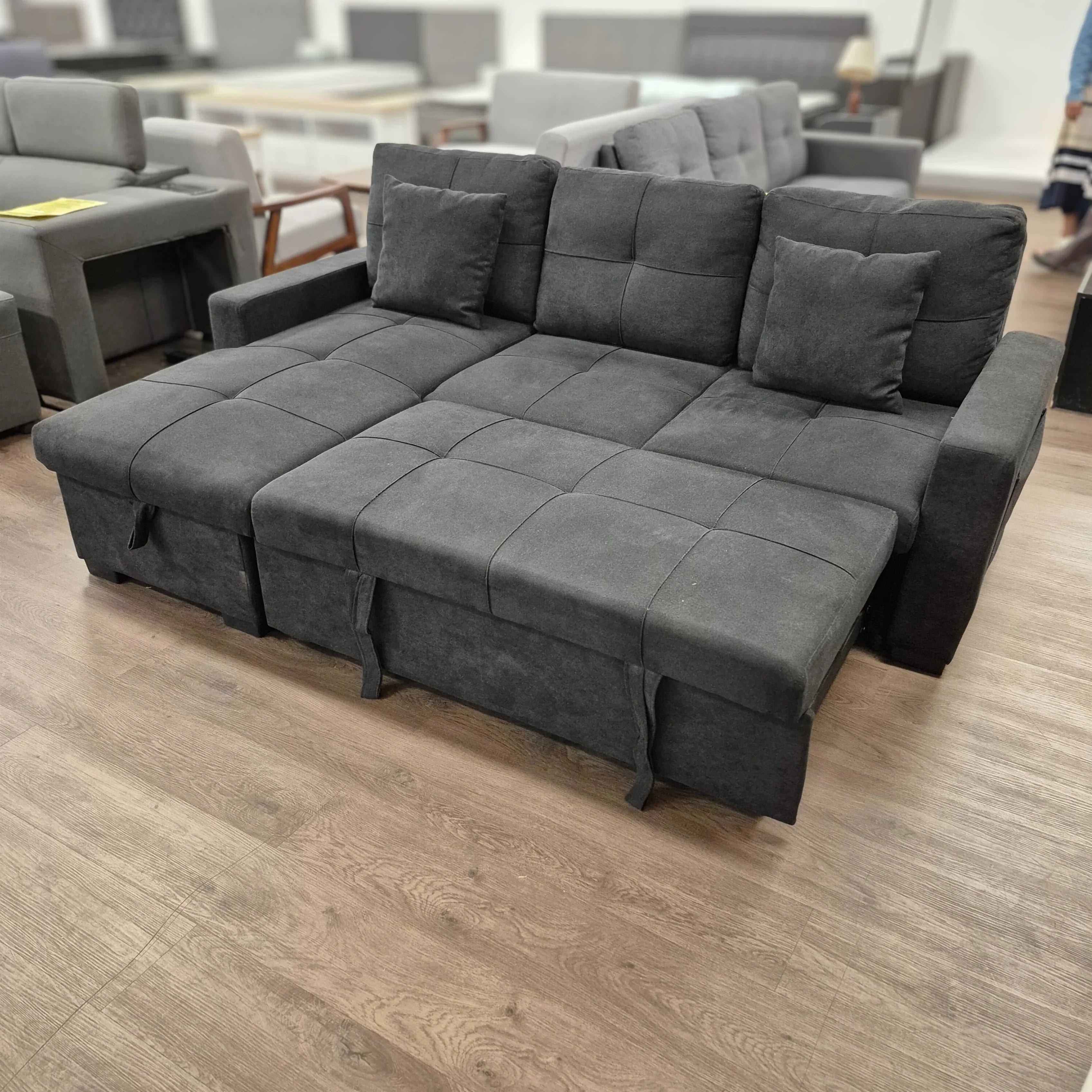 Black fabric pull-out sofa bed with cushions, displayed in a modern furniture showroom