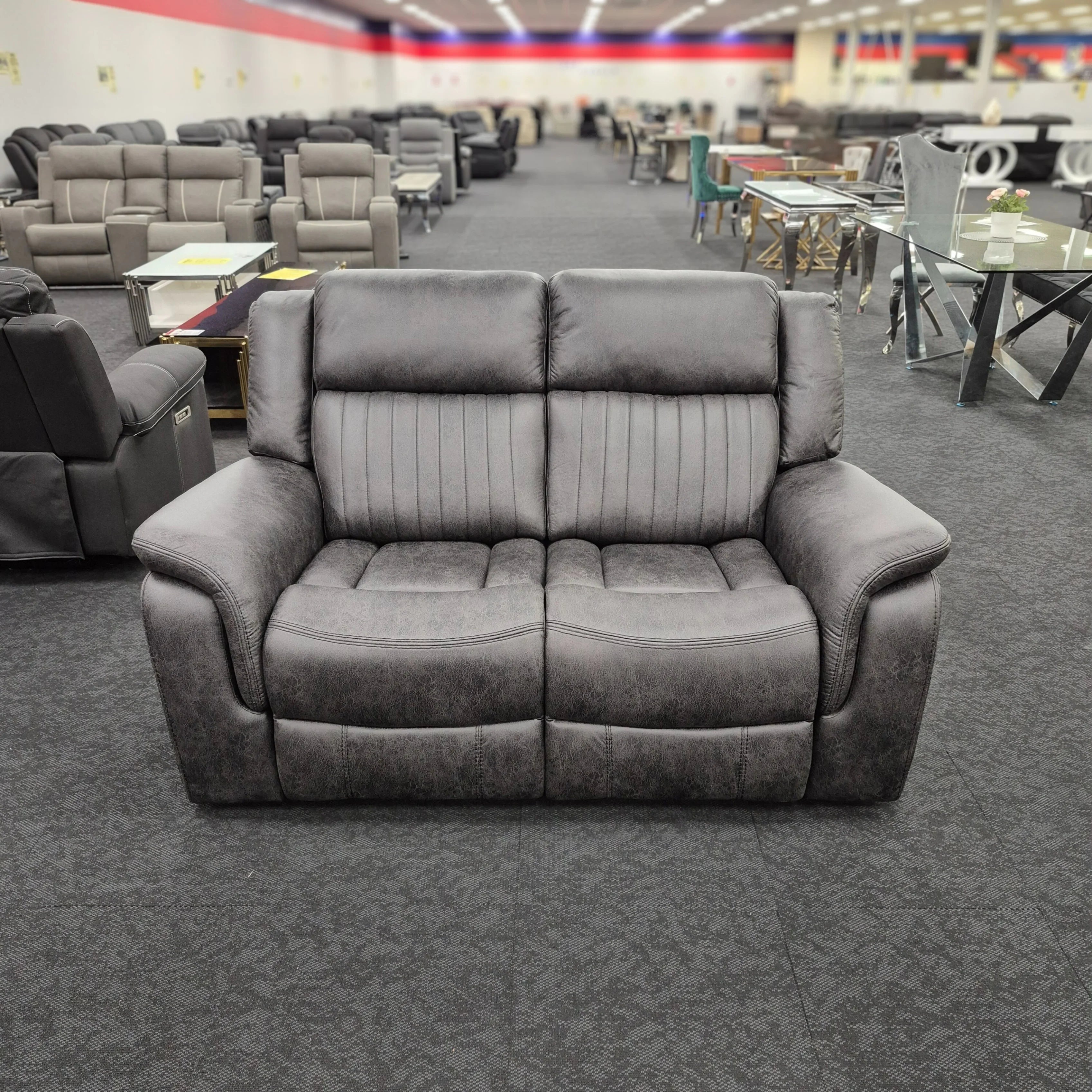 Grey two-seater recliner lounge sofa in a showroom with other modern furniture displays