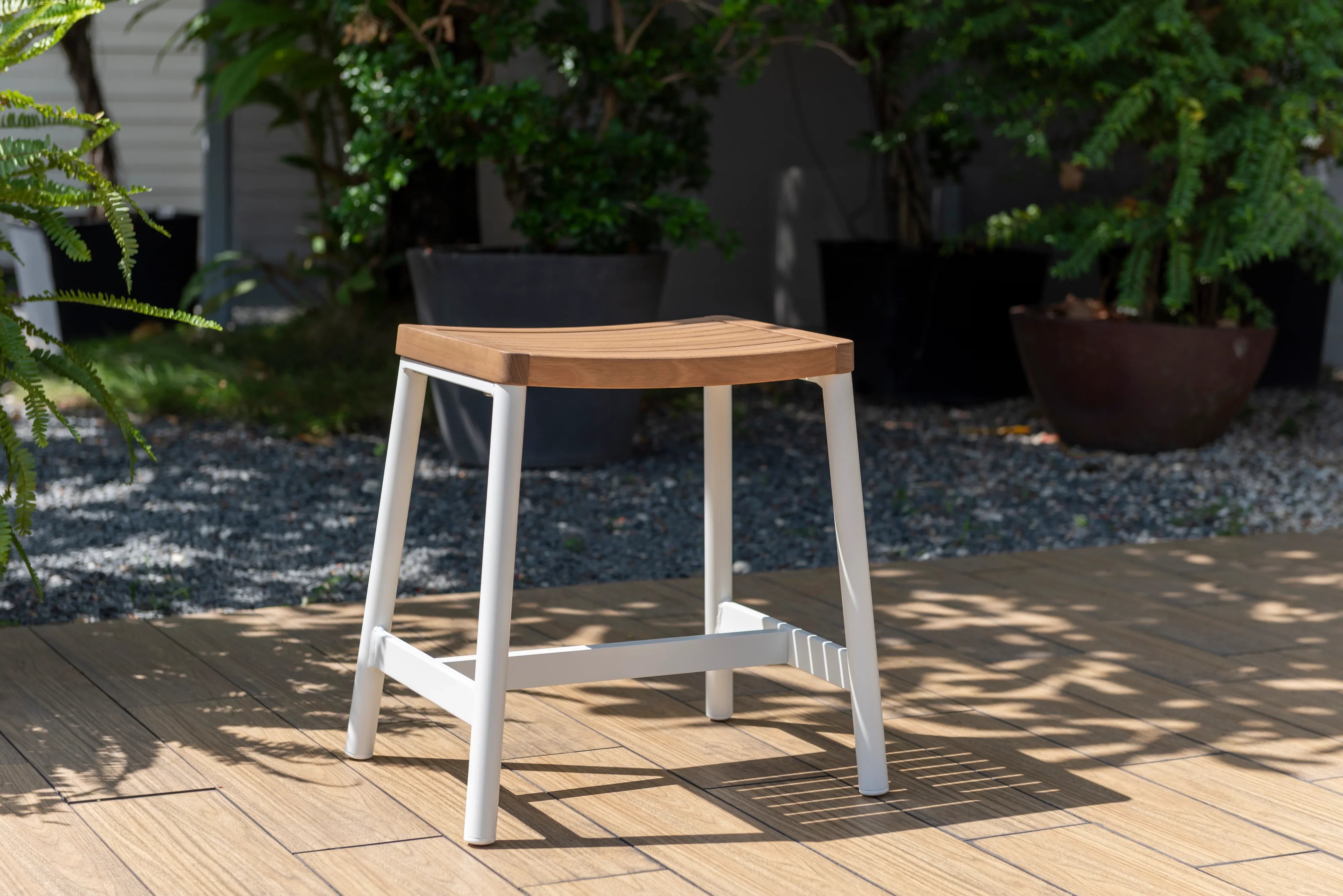 Outdoor wooden and metal stool on a patio with greenery in the background