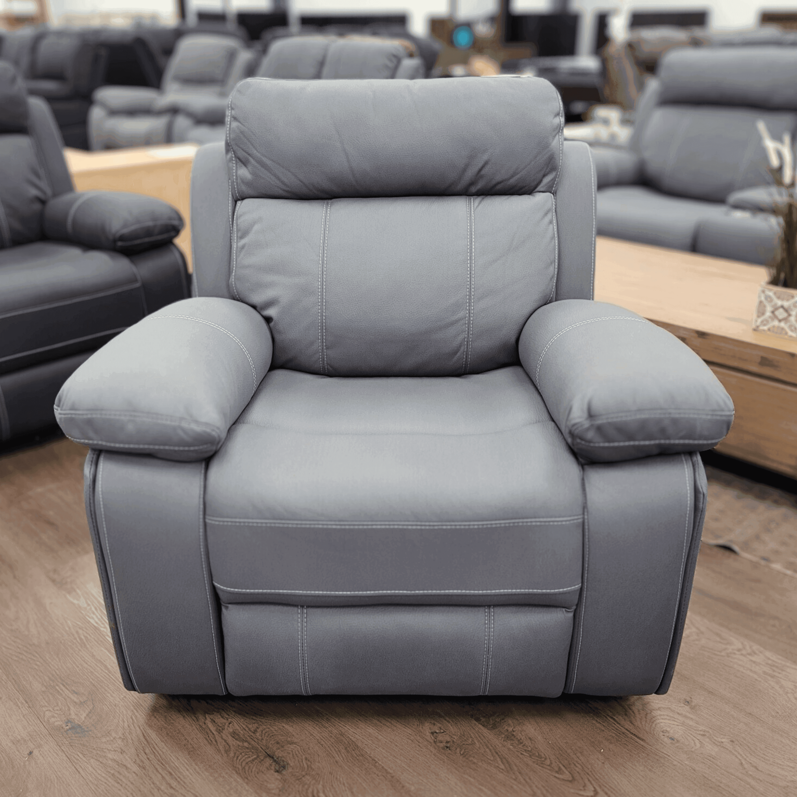 Gray leather recliner chair with padded armrests in a modern furniture showroom