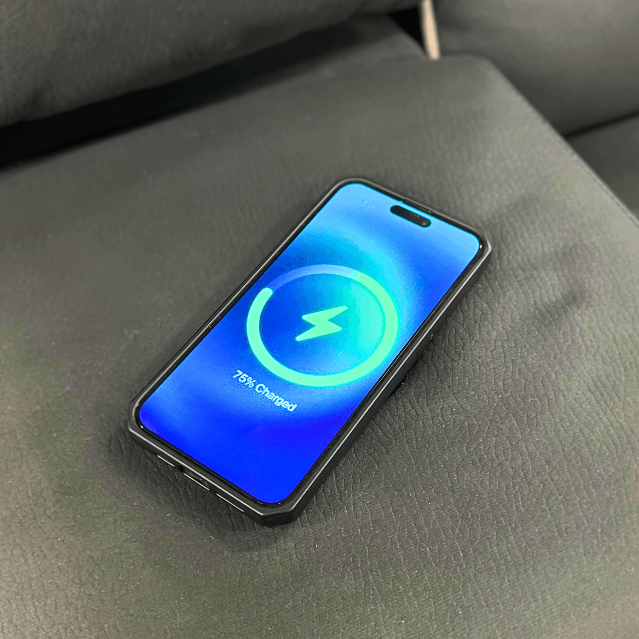 Smartphone charging wirelessly on grey leather sofa with 75% charged screen display