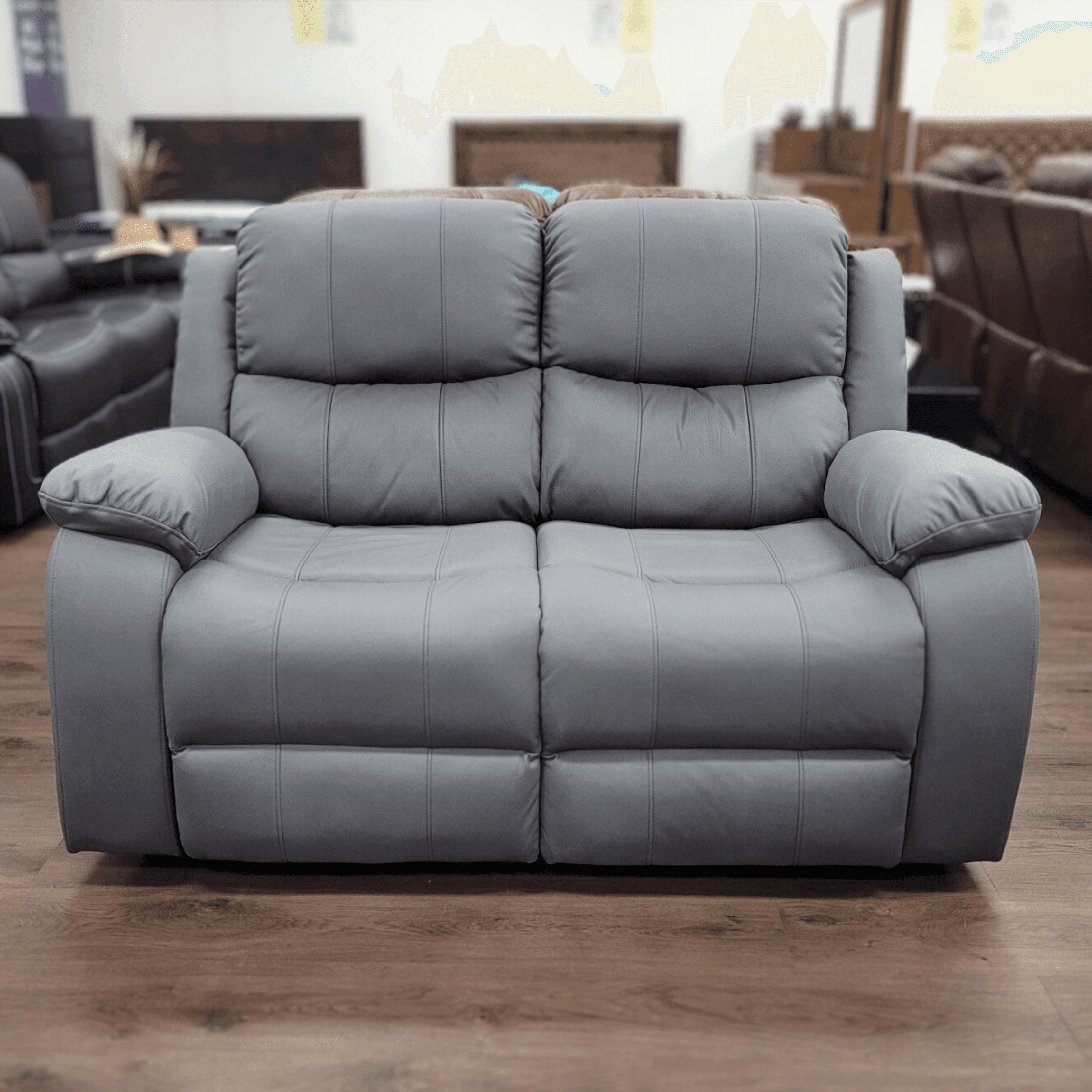 Grey 2-seater recliner lounge with plush cushions in a showroom on wood flooring