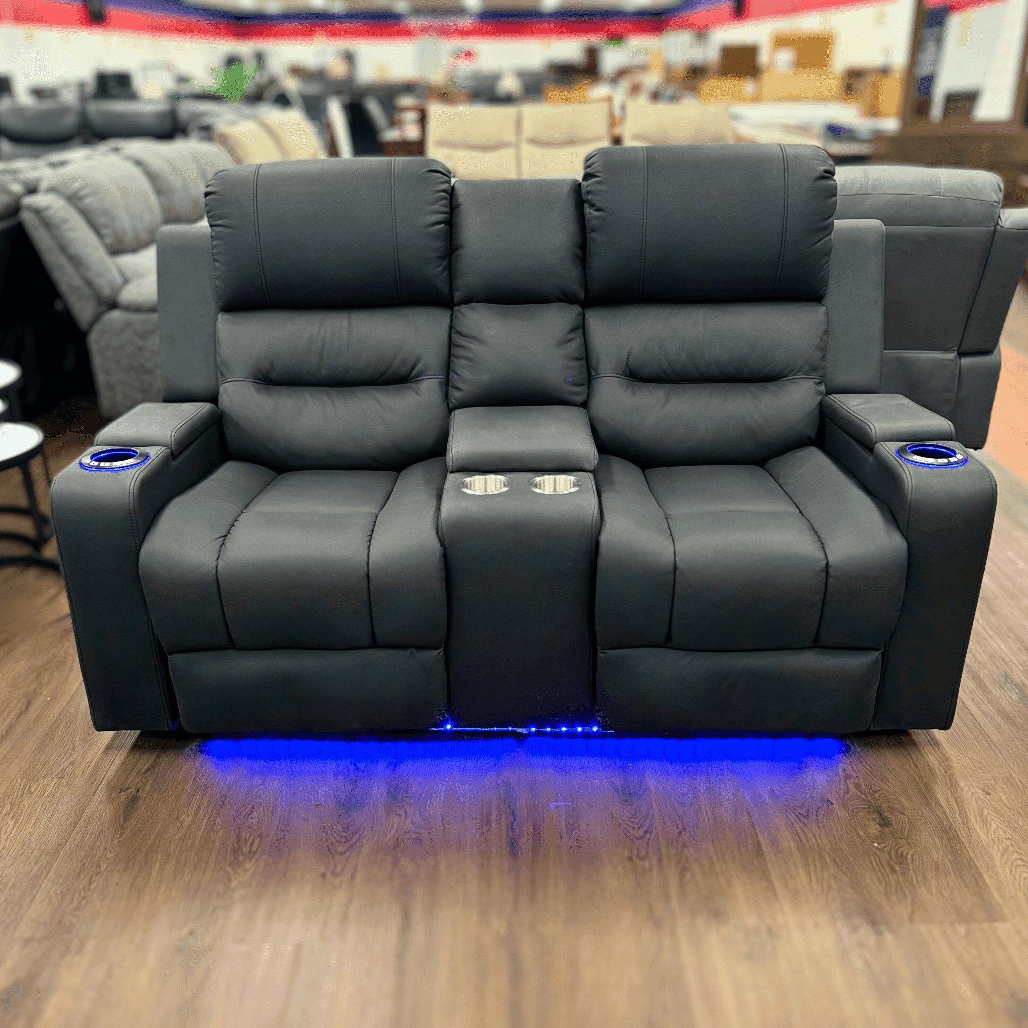 Black two-seater recliner lounge with cup holders and blue LED lighting, showroom display