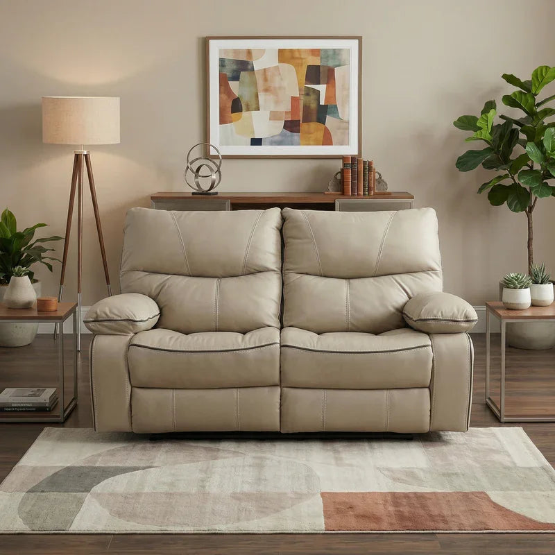 Brooke 2 Seater Recliner Lounge in beige leather with cushioned armrests and backrests, placed in a modern living room setting with abstract wall art, plants, and wooden furniture.