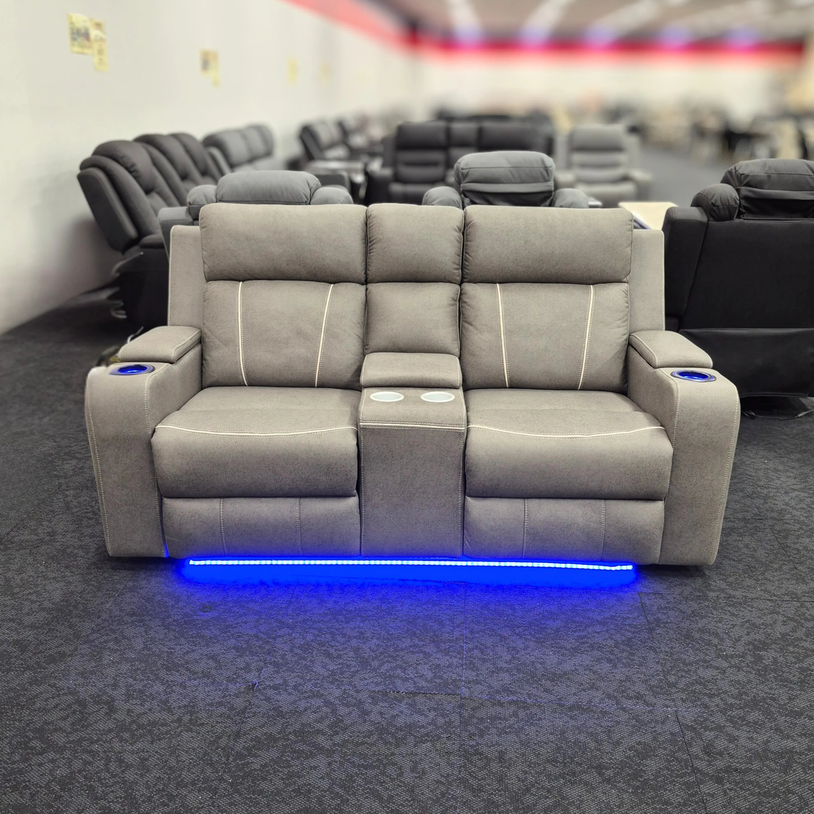 Grey two-seater recliner lounge with cup holders and blue LED lighting in a showroom