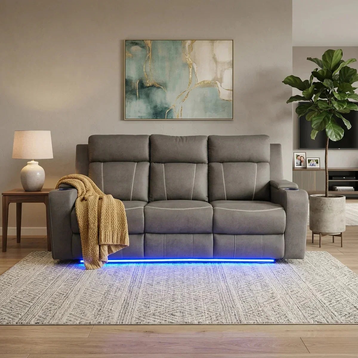 Modern grey Broom 3 Seater Electric Recliner Lounge with LED lighting underneath, placed in a cozy living room with a patterned rug, side table, lamp, and wall art.