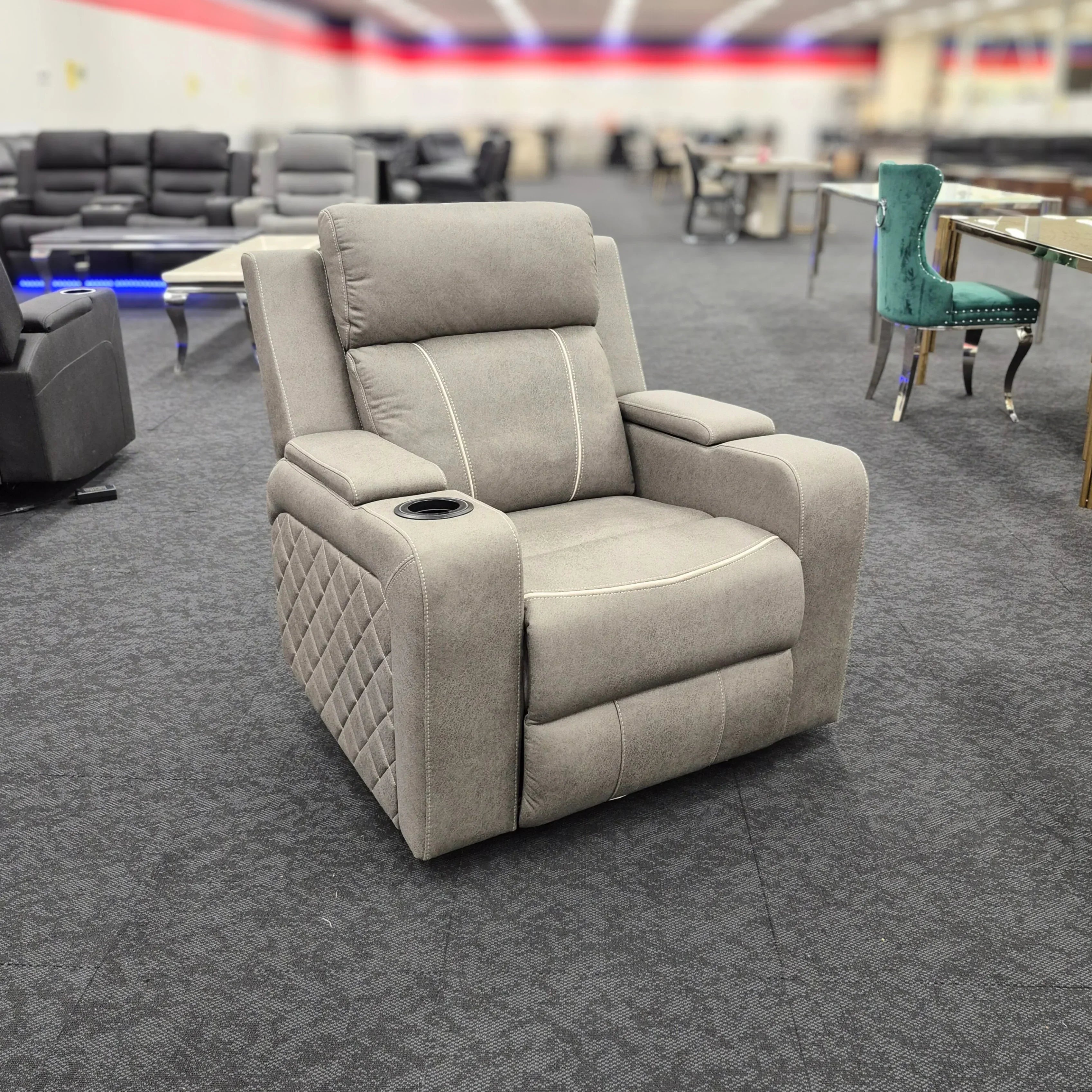 Modern grey fabric recliner chair with cup holder and quilted side in a furniture showroom