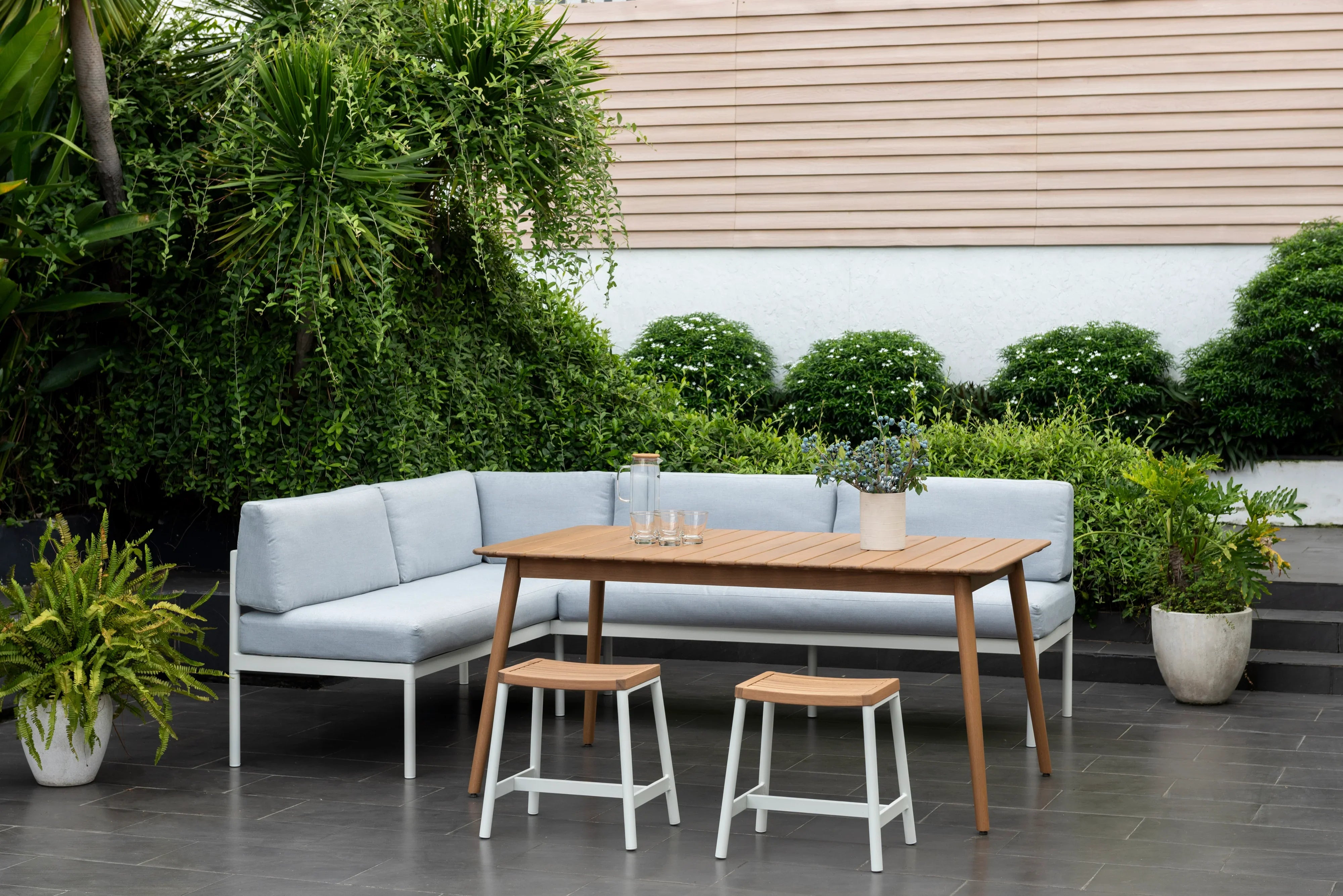 Outdoor corner lounge set with light grey cushions, wood dining table, and stools on patio