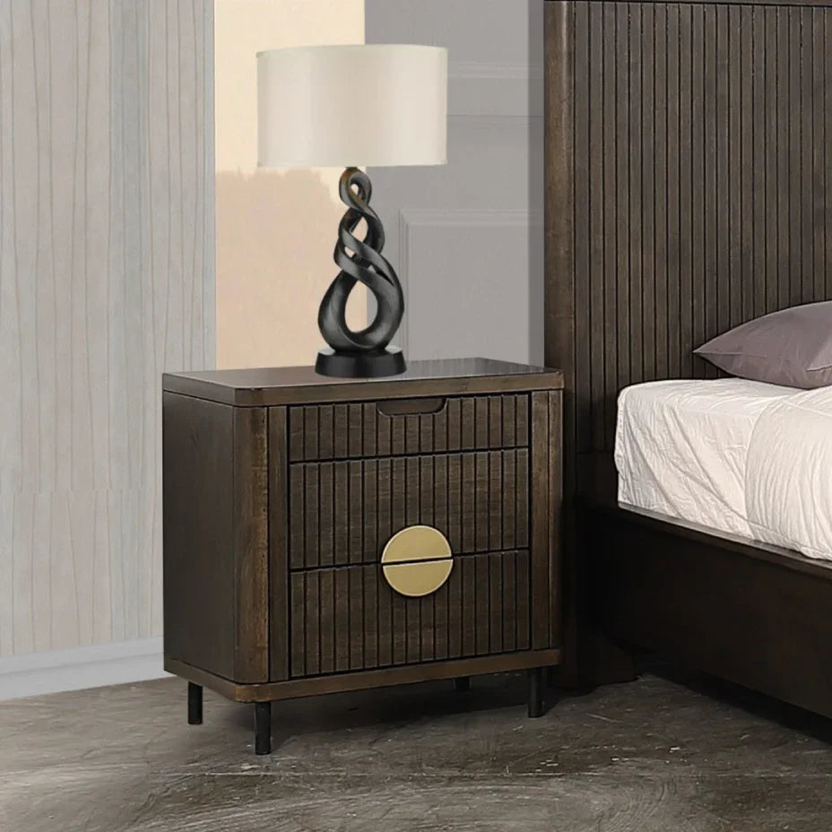 Wooden nightstand with a lamp and decorative object next to a bed in a bedroom setting.