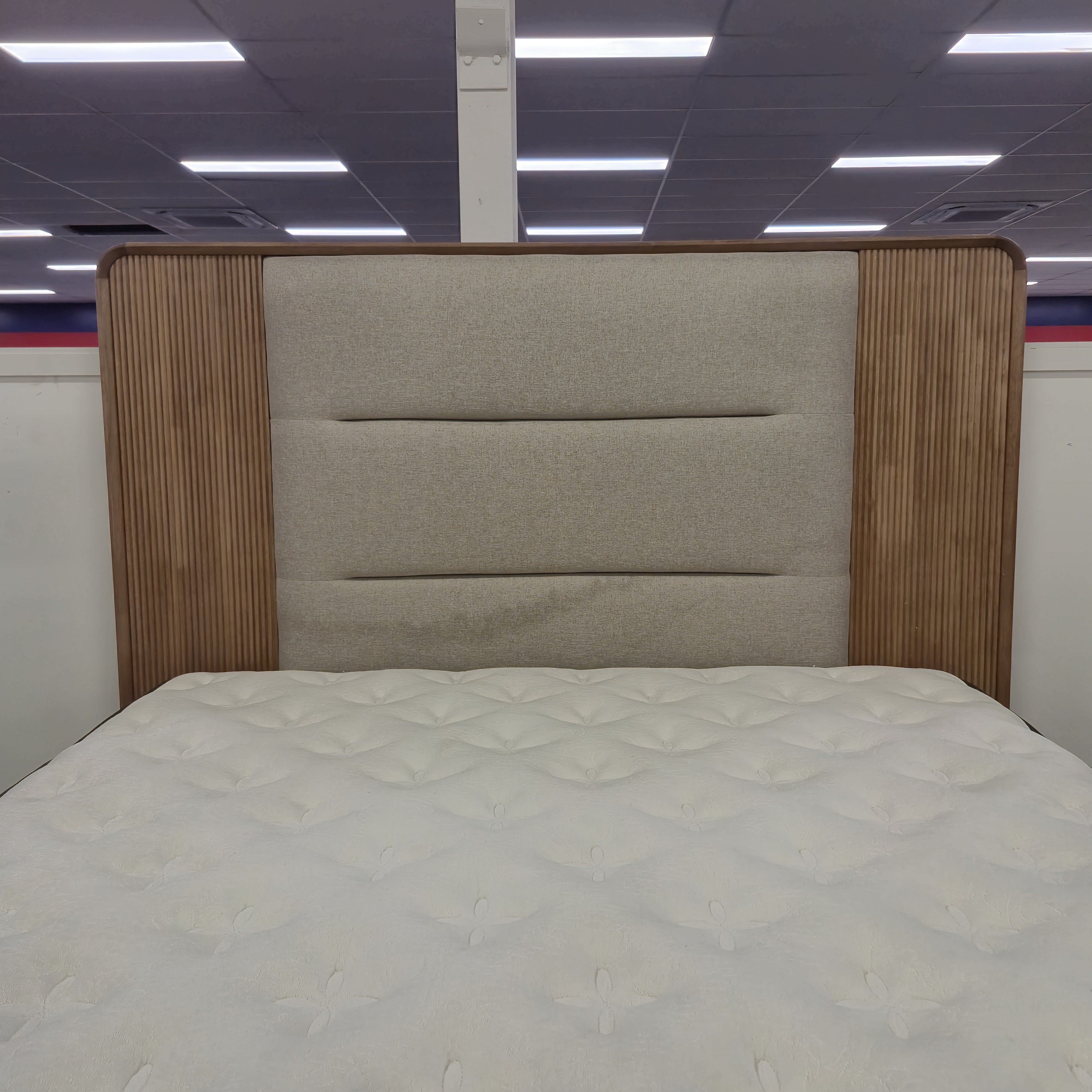 Headboard of the Castle Bed Frame, with a beige upholstered centre panel in horizontal channels flanked by fluted natural timber wing panels, in The A2Z Furniture showroom. Mattress shown is not included.