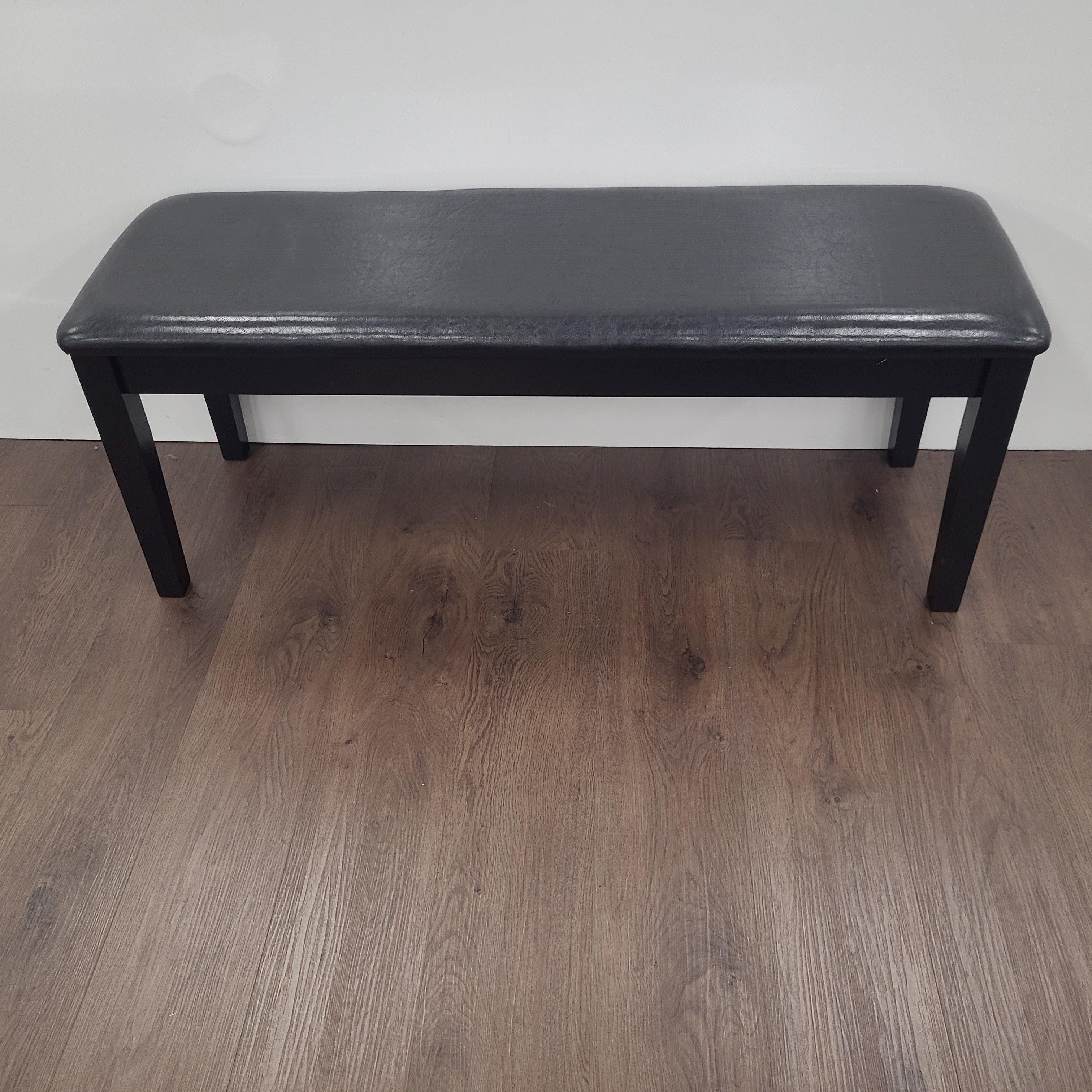 Modern black dining bench with cushioned seat on wood floor against white wall