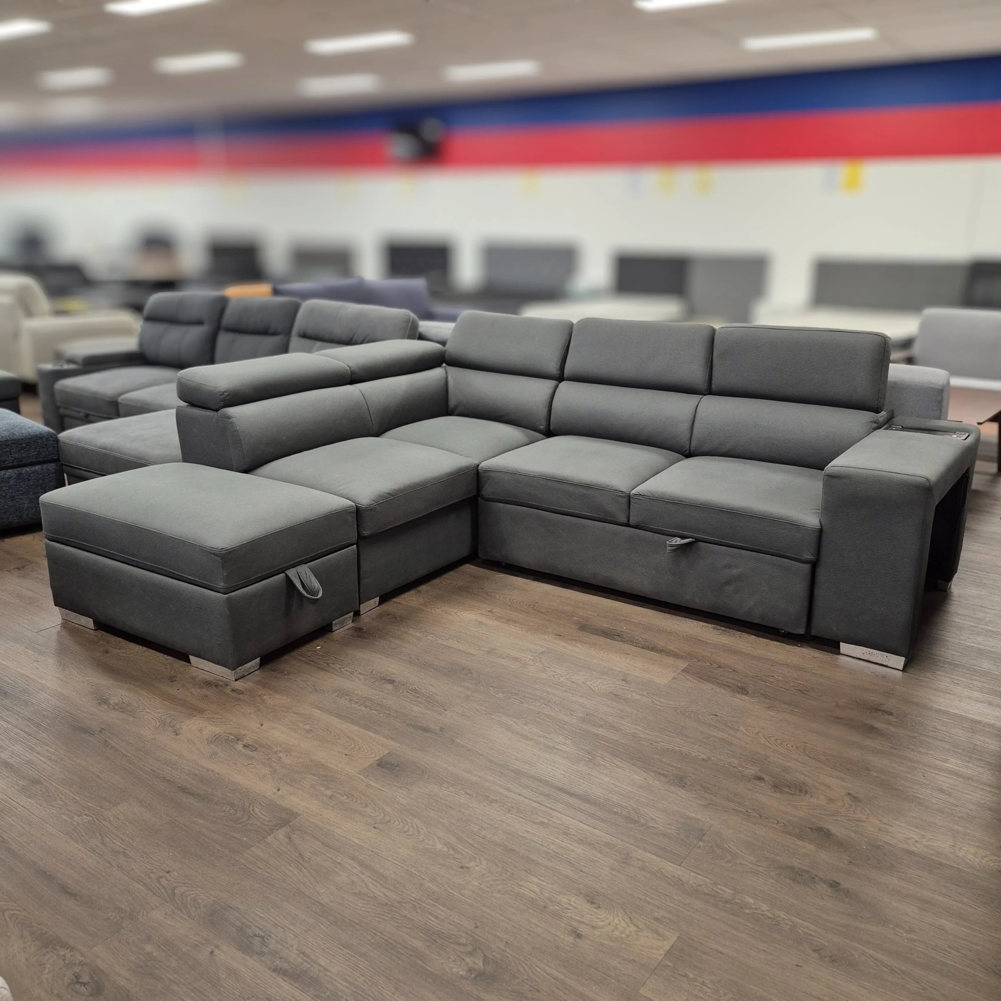 Modern grey L-shaped pull-out sofa bed with adjustable headrests in showroom on wood floor
