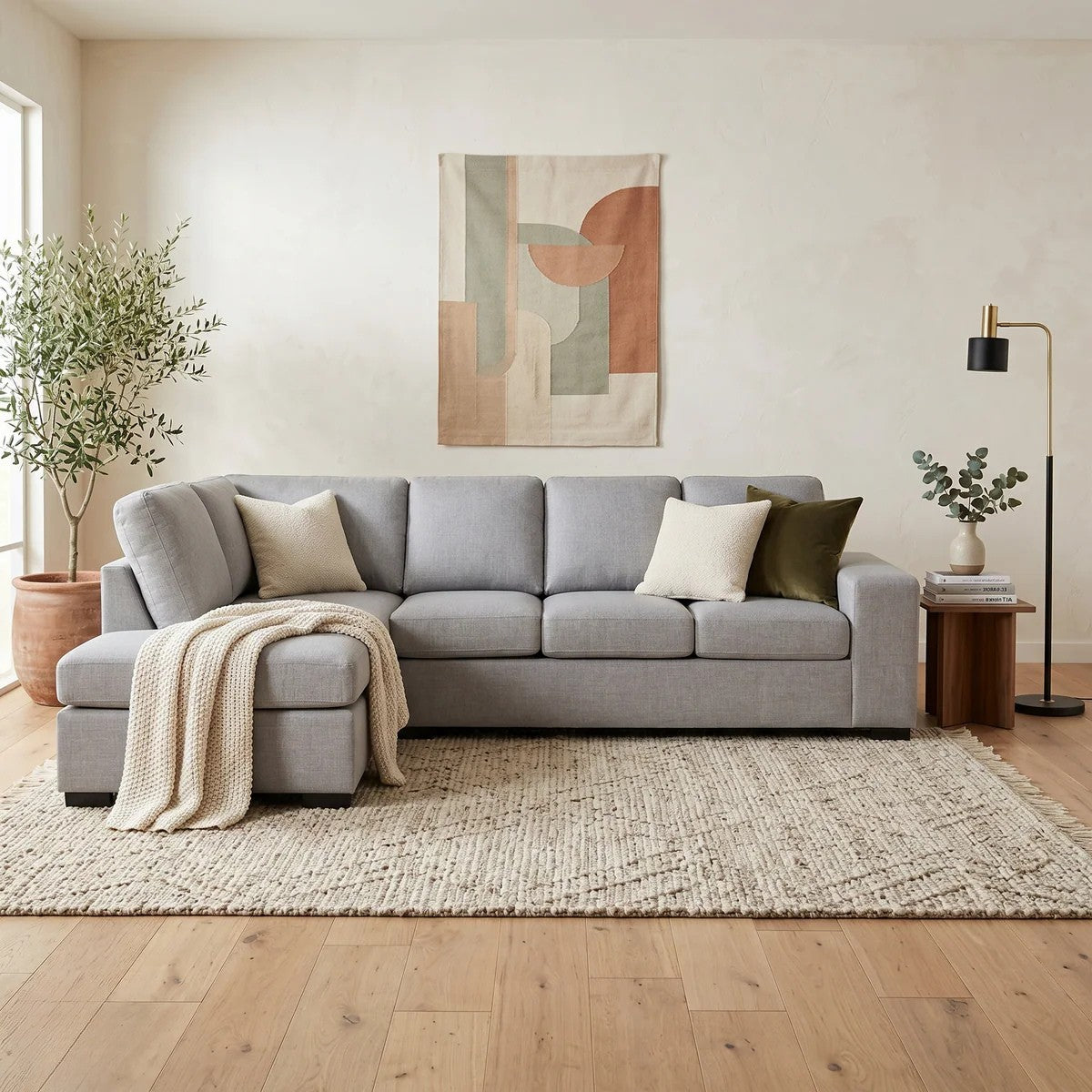 Fairfield Corner Sofa in light gray fabric with clean lines and plush cushions, styled with neutral throw pillows and a knit blanket in a bright, modern living room setting.