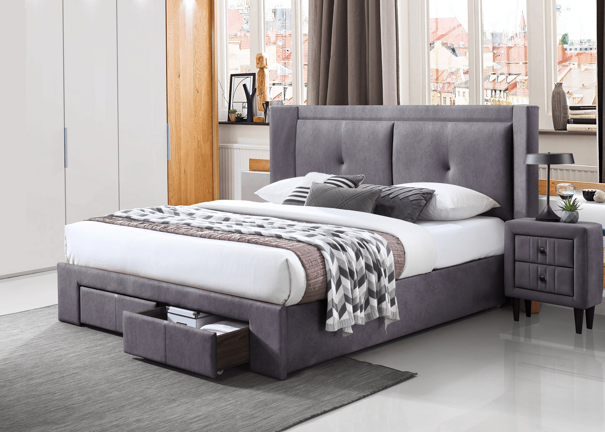 Modern grey upholstered bed with storage drawers, matching nightstand, and accent pillows in a bright bedroom