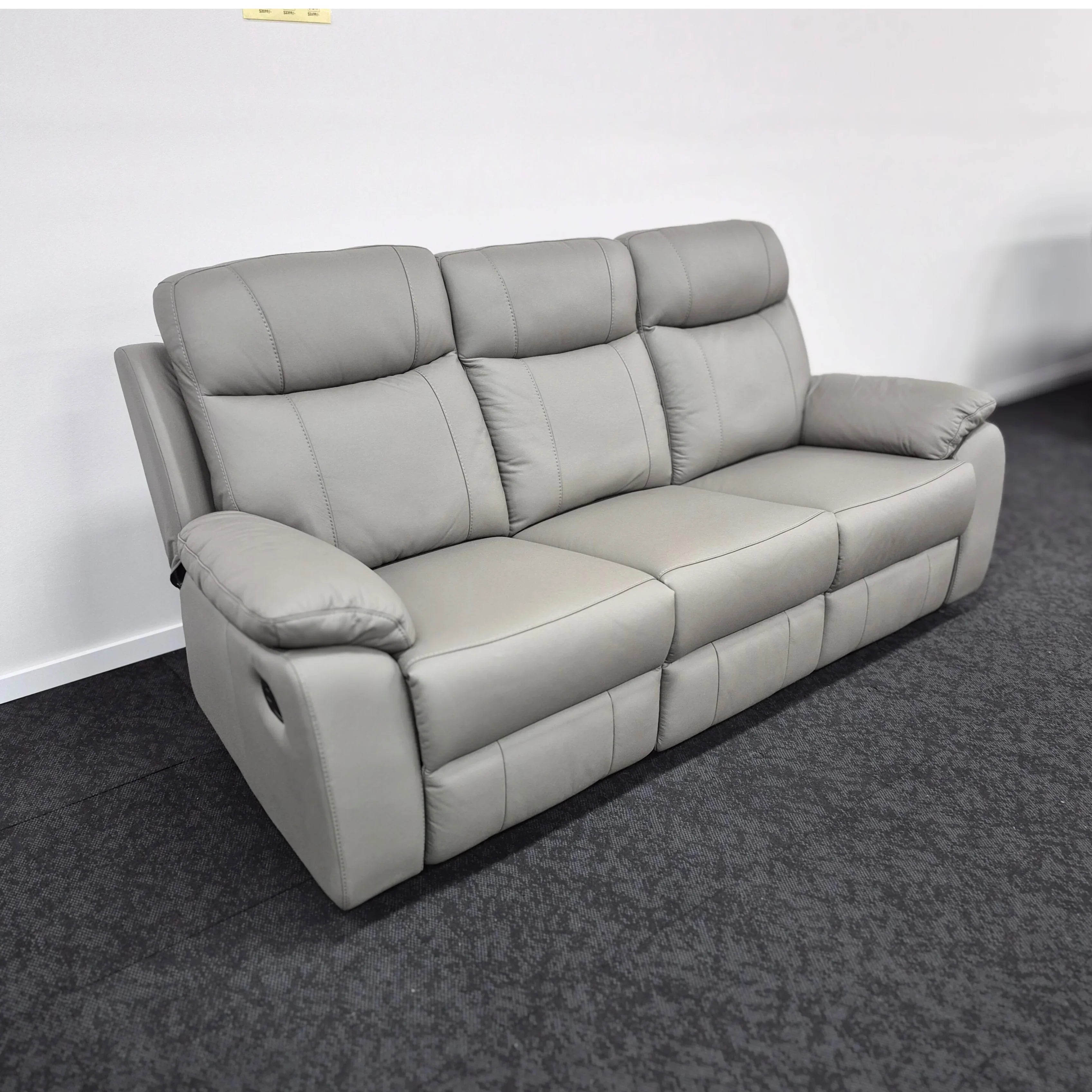 Grey leather 3 seater recliner sofa with plush cushions on dark carpeted floor