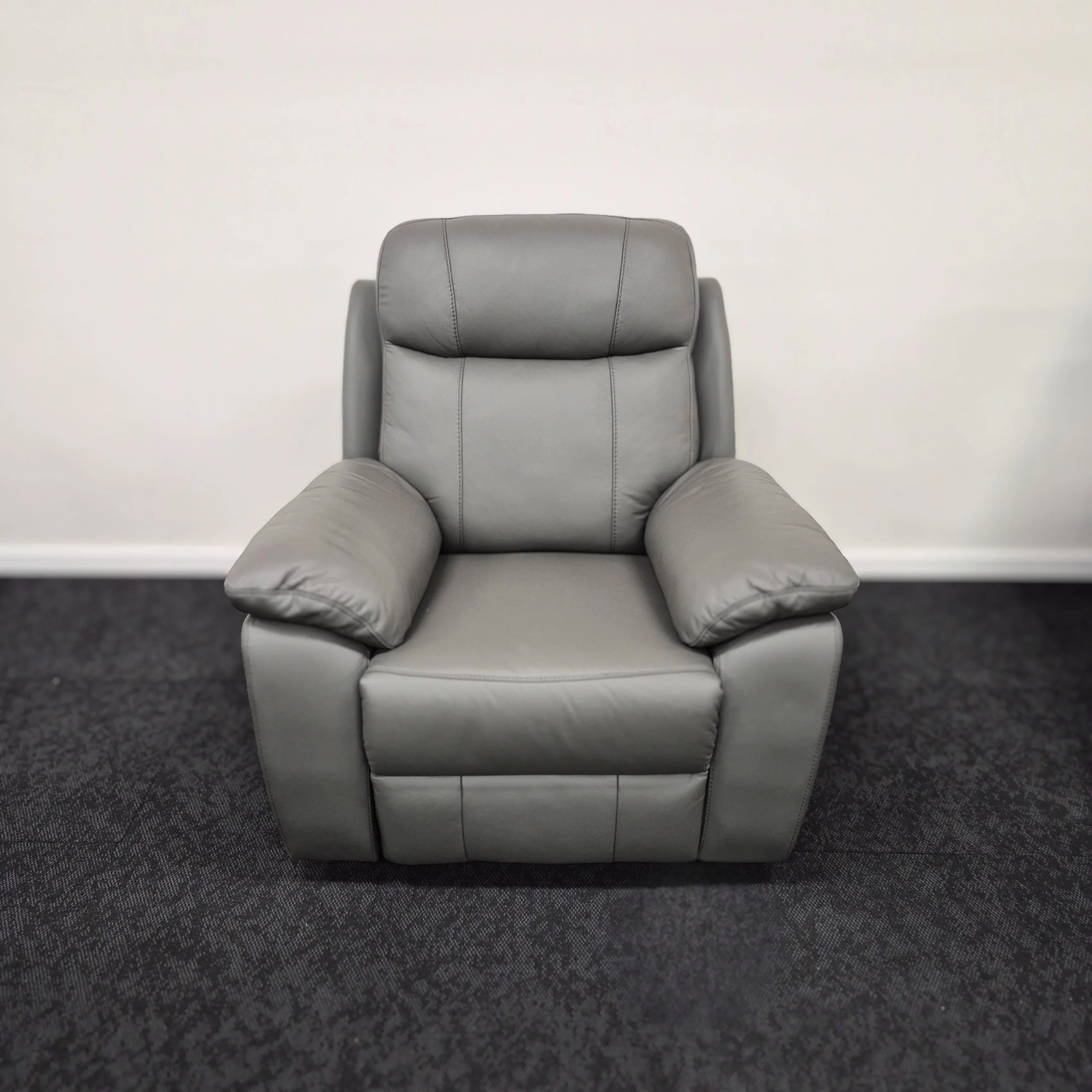 Grey leather single recliner armchair with padded arms and backrest on dark carpet