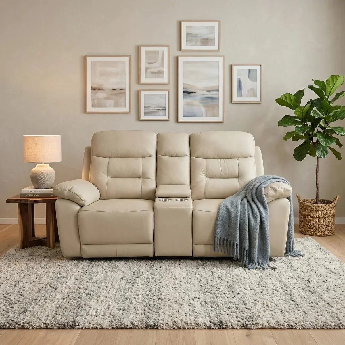 Beige reclining sofa in a living room with framed artwork on the wall and a plant.
