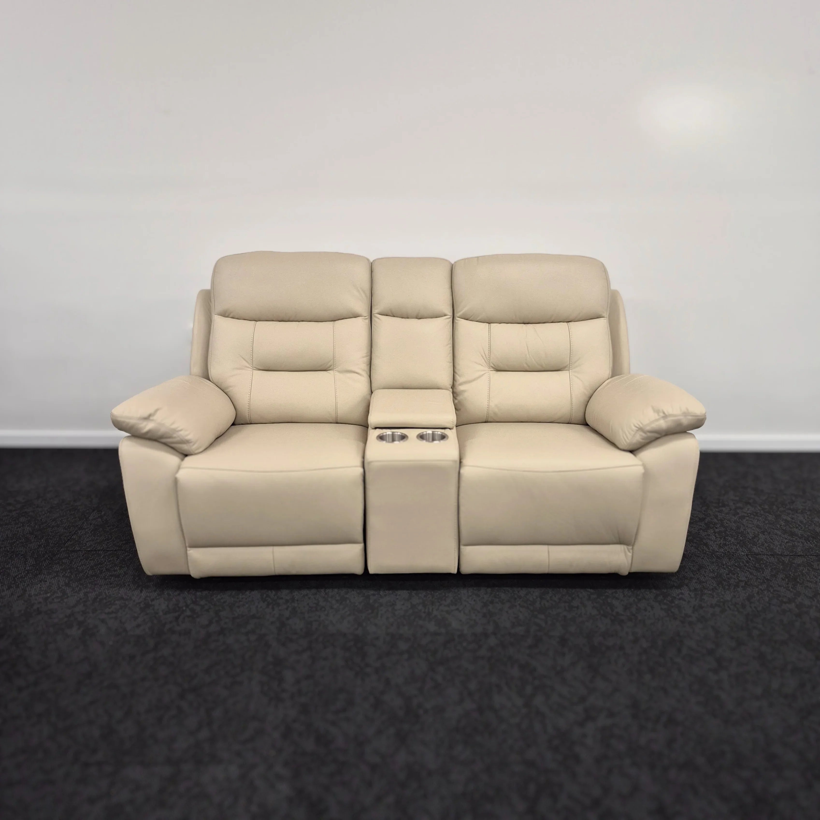 Beige leather two-seater recliner sofa with center console and cup holders on dark carpet