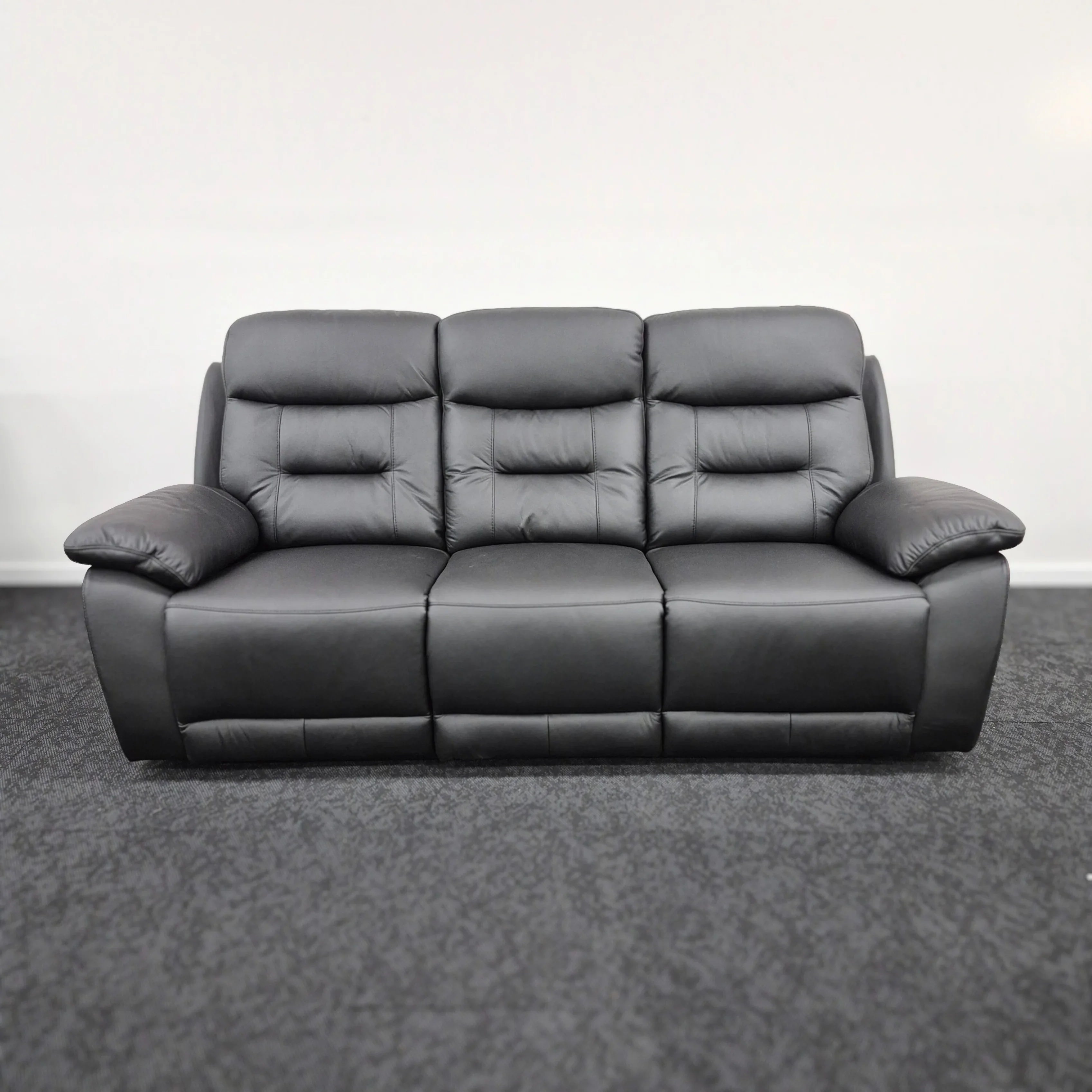 Modern three-seater black leather recliner sofa with wide armrests on carpeted floor