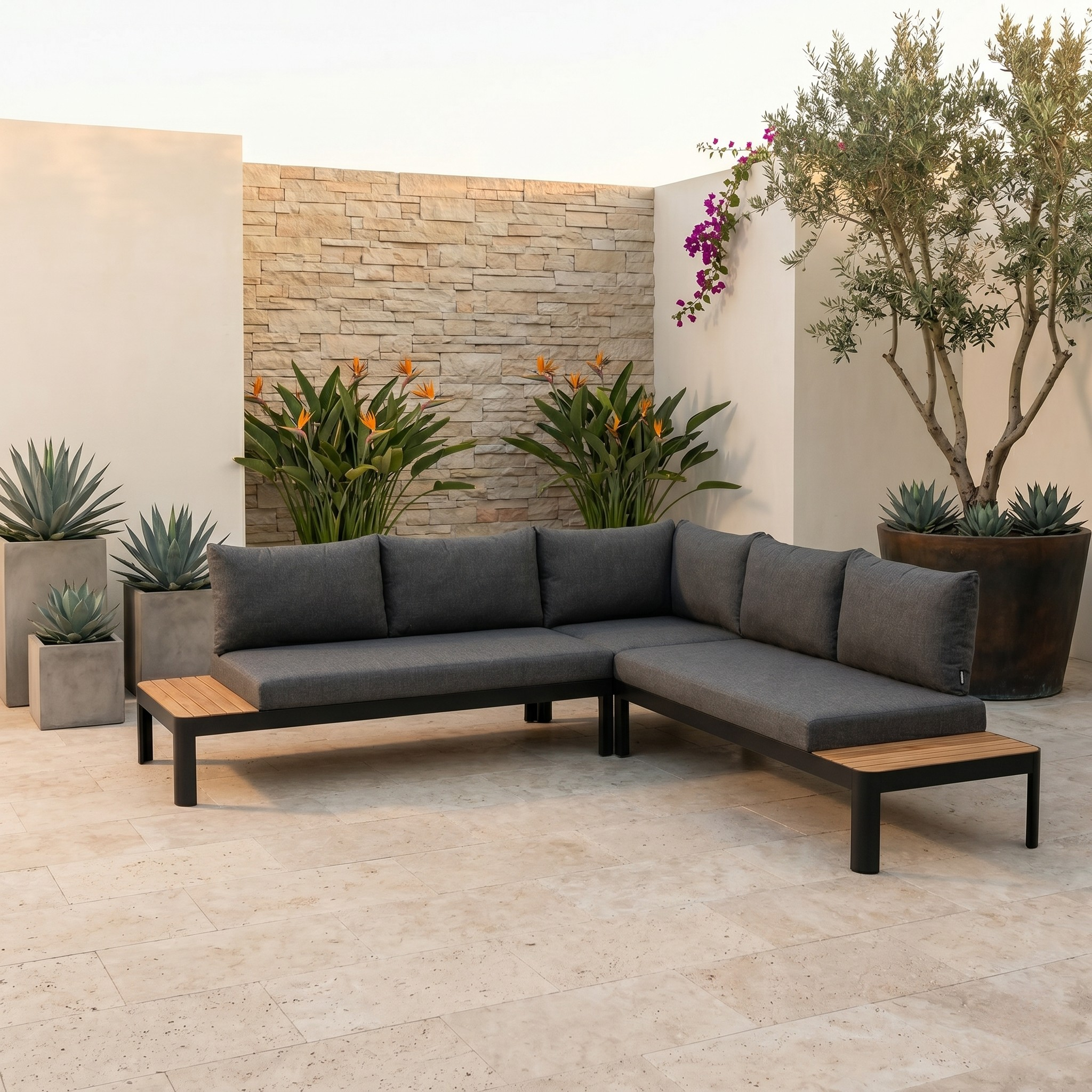 Gray sectional sofa with wooden coffee table in an outdoor setting with plants and stone wall.