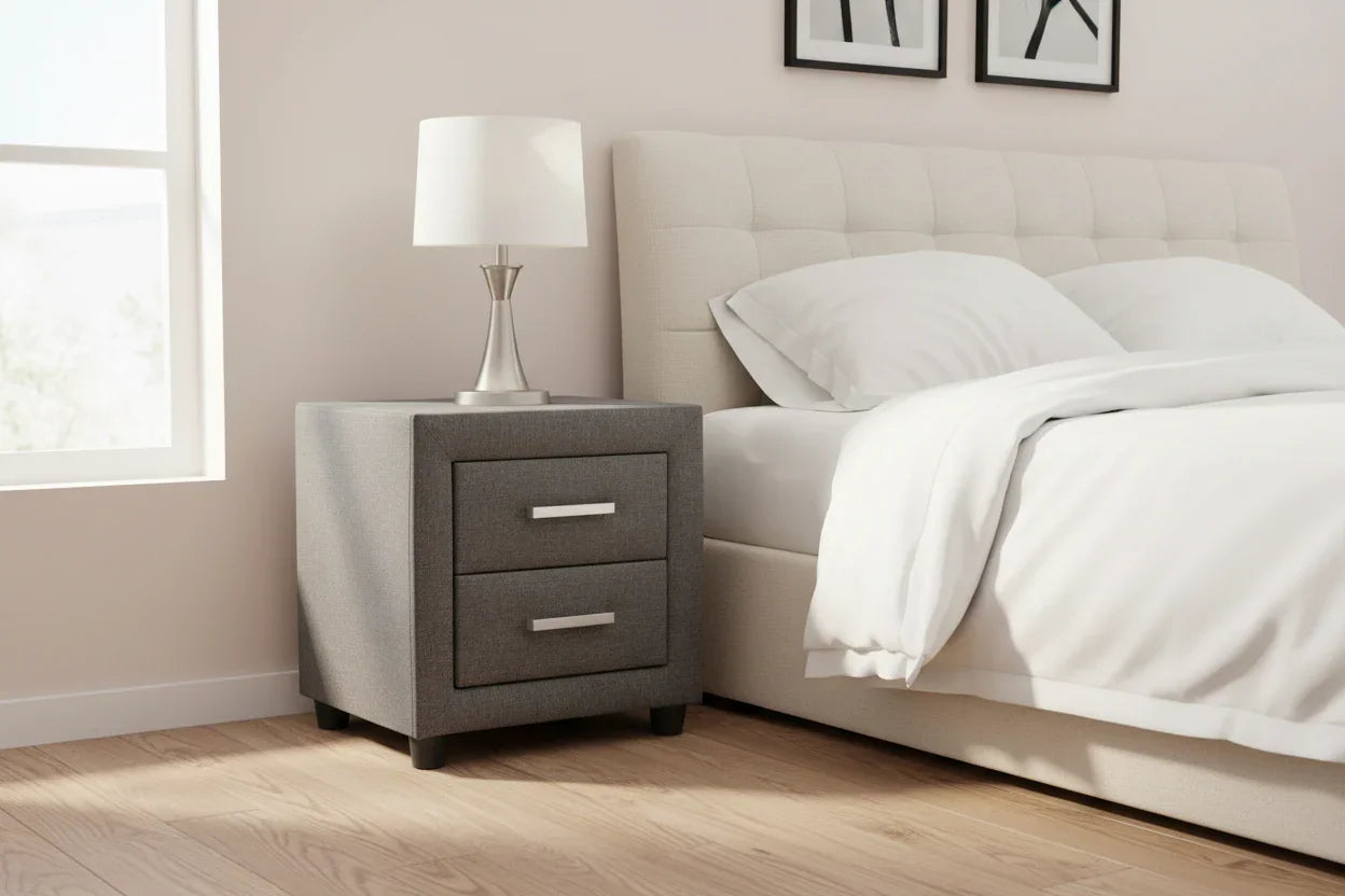 Grey fabric bedside table with two drawers beside a modern bed in a bright bedroom