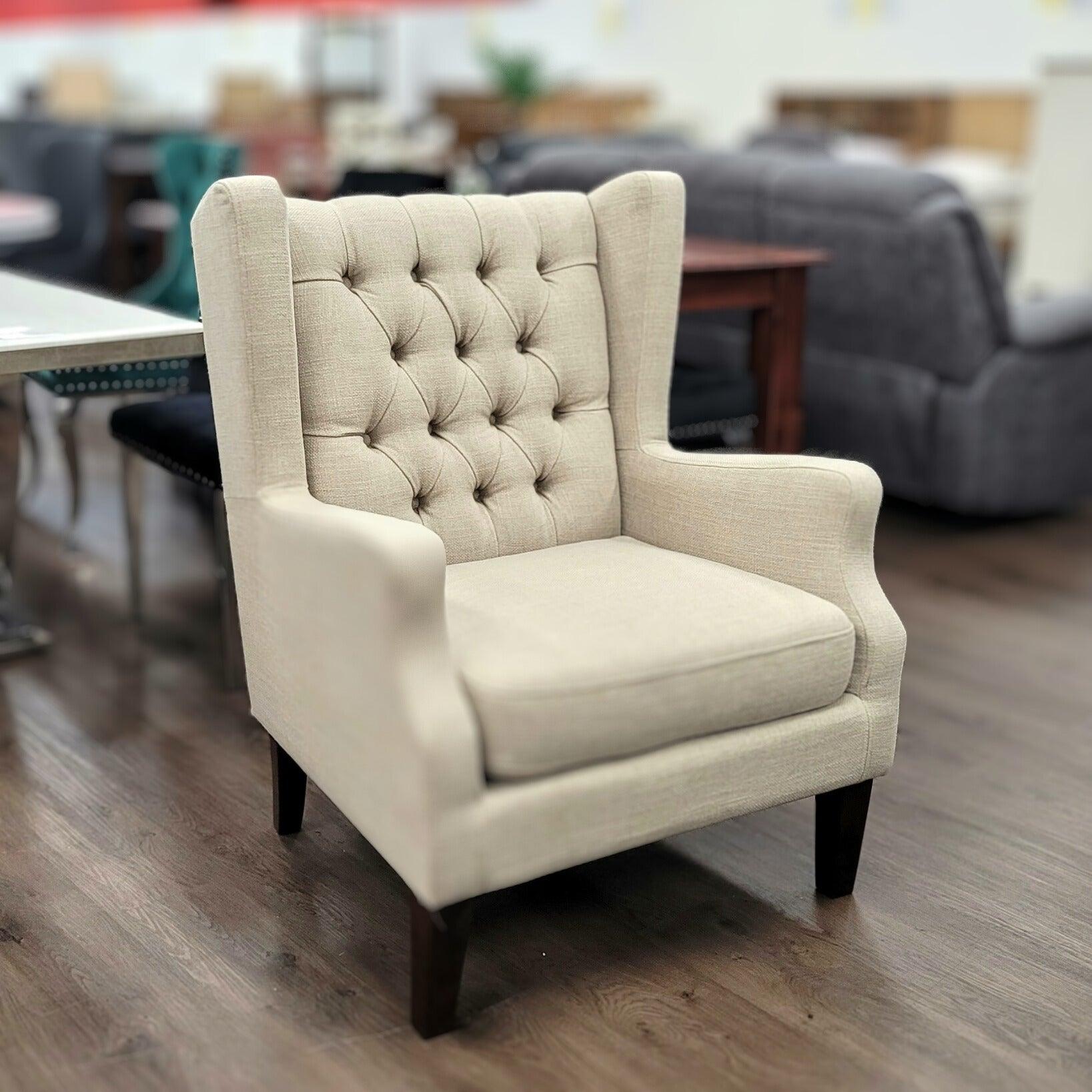 Beige tufted armchair with high backrest and wooden legs on showroom floor