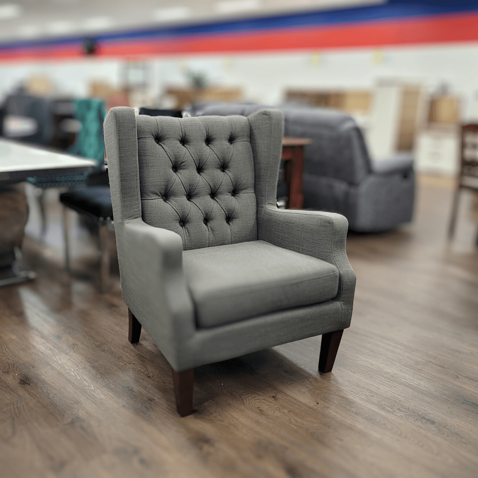 Grey tufted accent armchair with wooden legs on a showroom floor