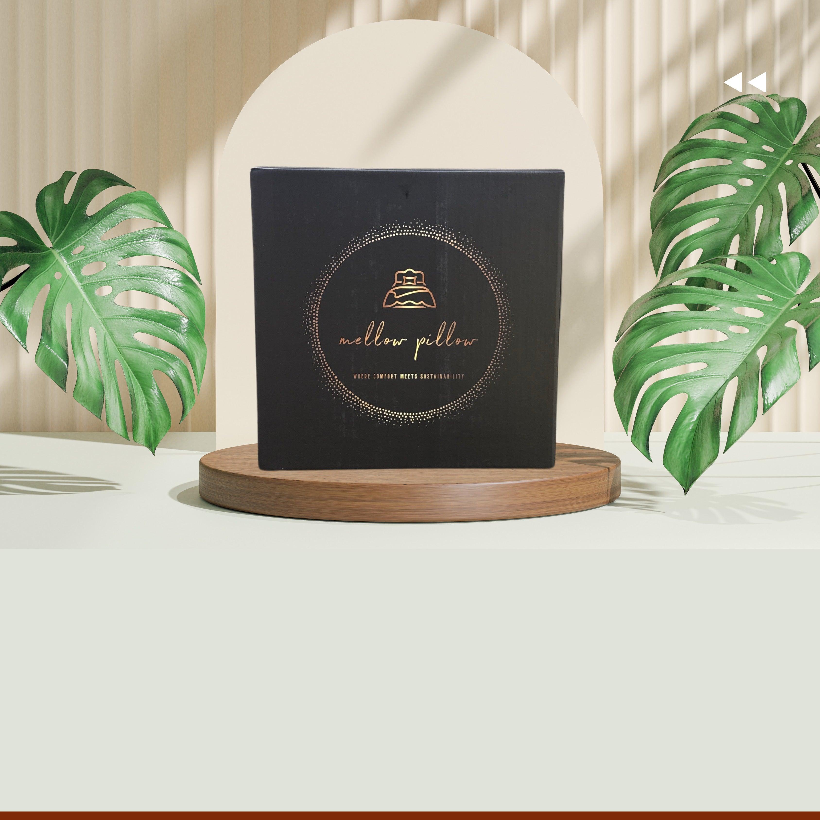 Modern pillow packaging box on wooden display, surrounded by green leaves, neutral decor