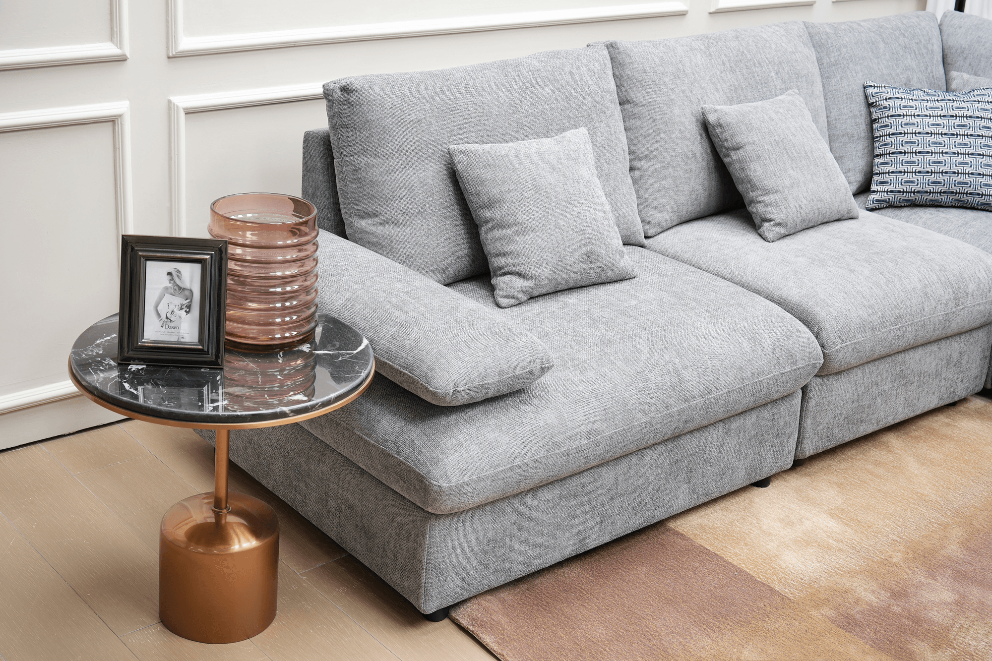 Modern grey sectional sofa with decorative cushions beside a black marble and gold side table