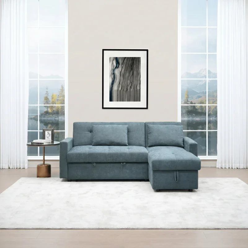 Oasis Pull Out Sofa Bed in blue fabric with chaise lounge, set in a bright living room with large windows, a modern side table, and white curtains.