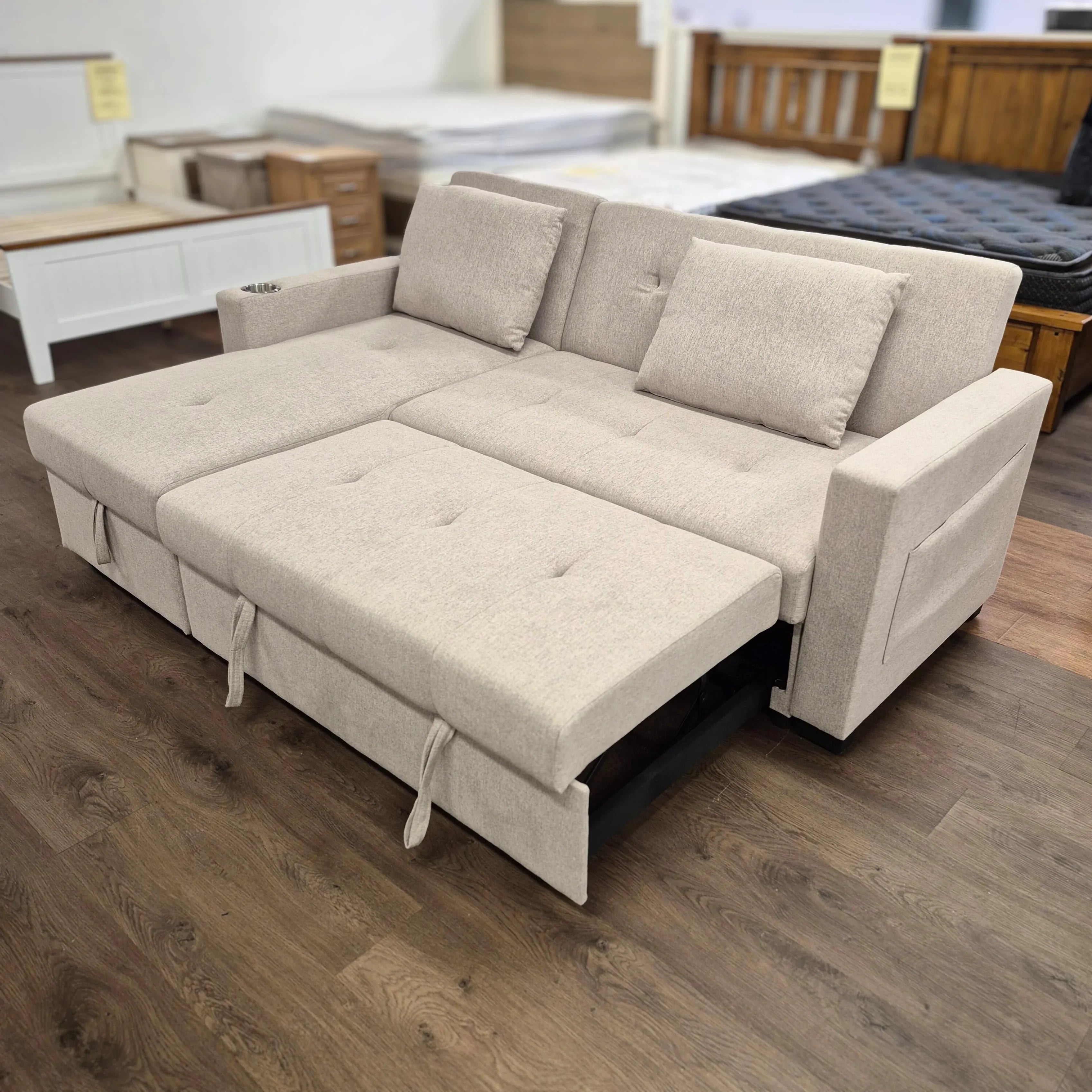 Beige sofa bed pulled out in furniture showroom, modern design with cushions and storage.