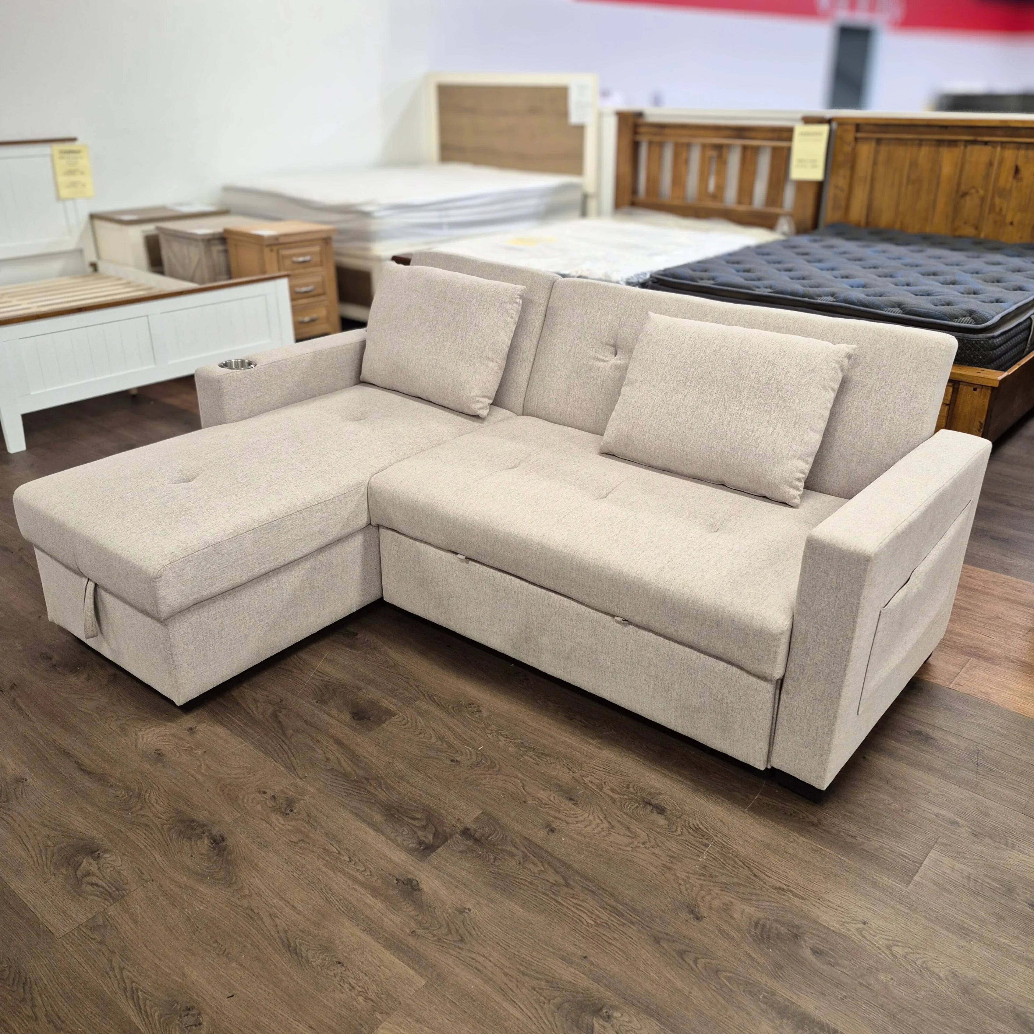 Beige L-shaped sofa bed with cushions in a furniture showroom on wood flooring