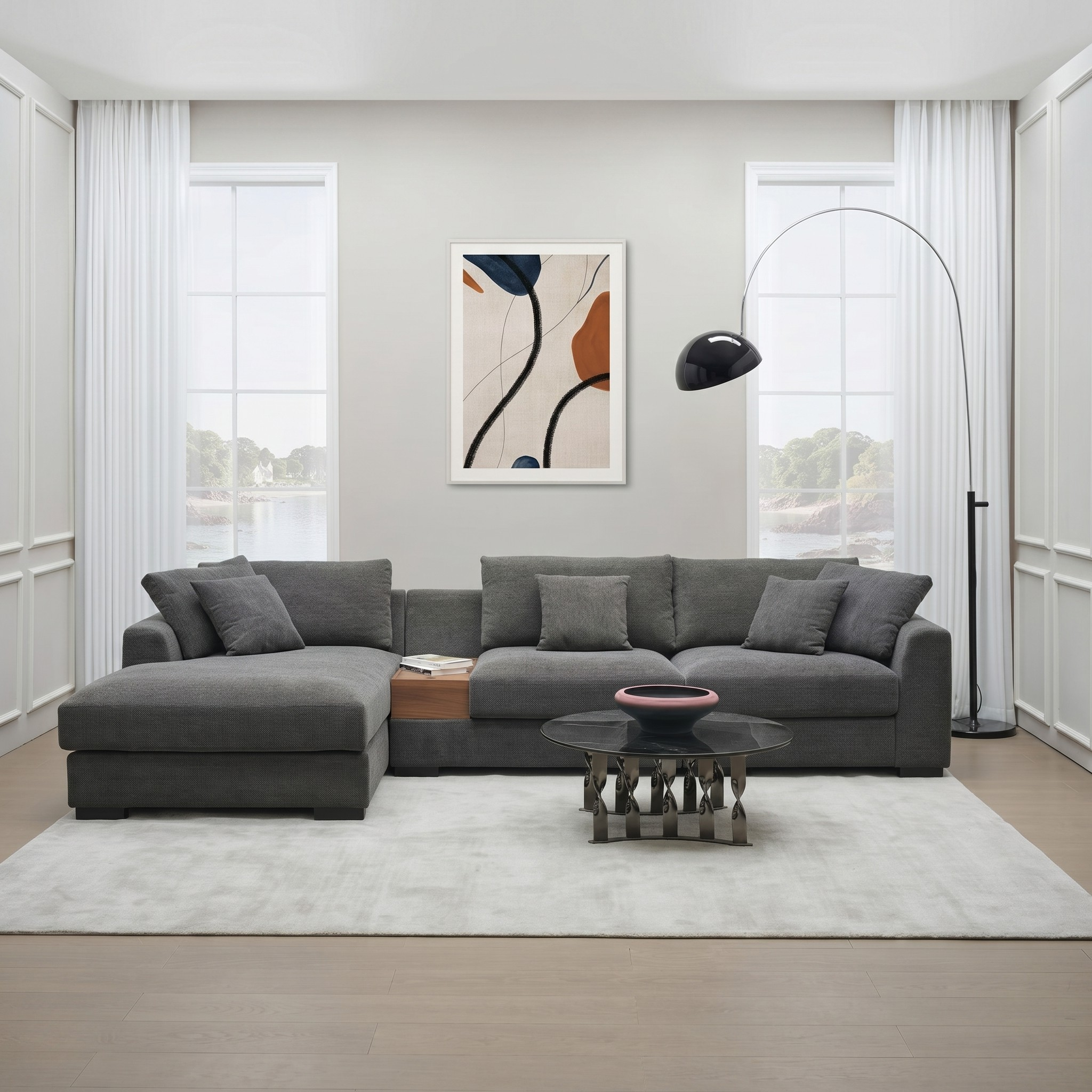 Odessey 3 Seater Chaise Sofa in dark gray fabric with plush cushions, featuring a built-in wooden side table, placed in a modern living room with large windows and a floor lamp.