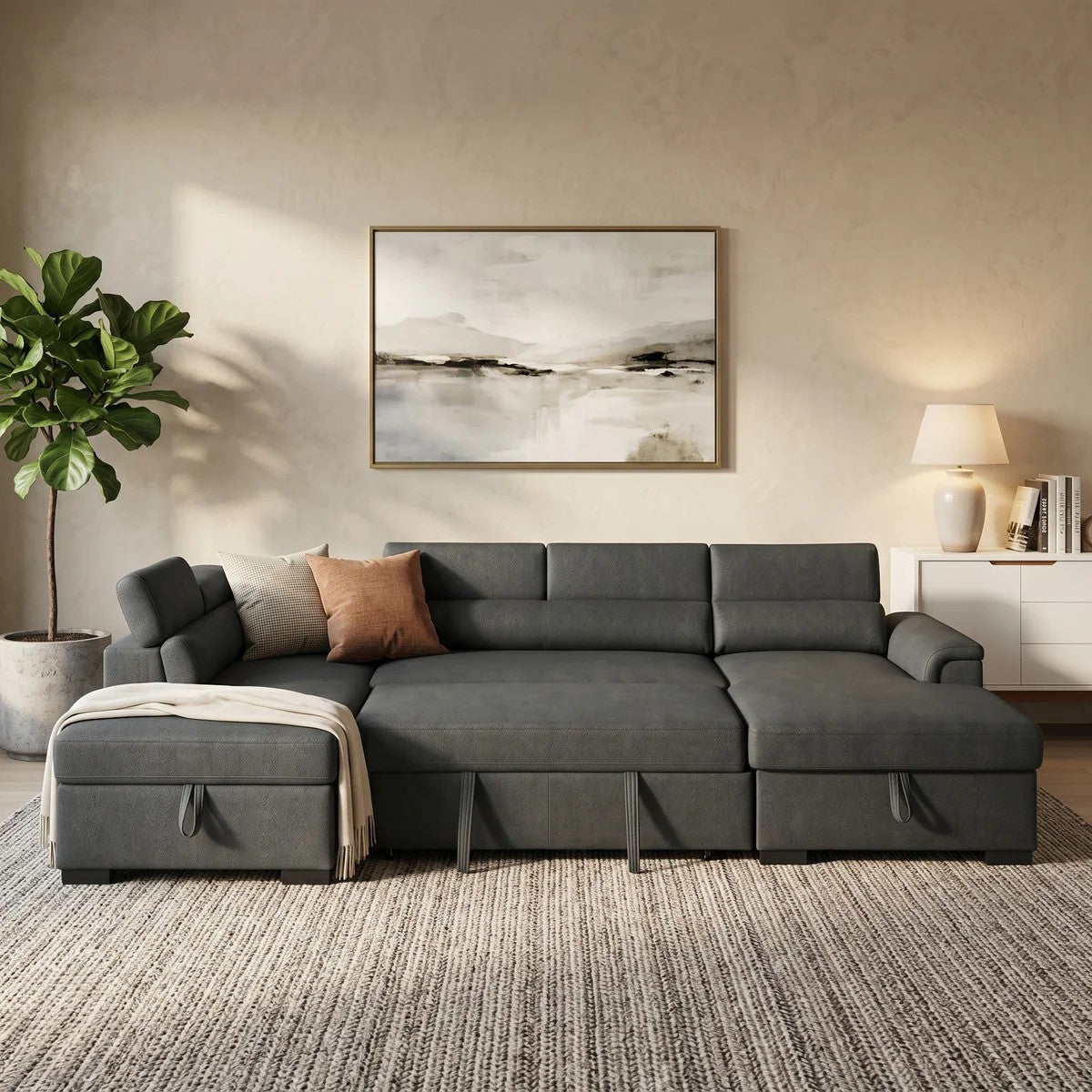 Contemporary living room featuring a dark gray Omaha Pull-Out Sofa Bed with plush cushions, a chaise lounge, and neutral-toned decor including a houseplant, abstract wall art, and a table lamp.