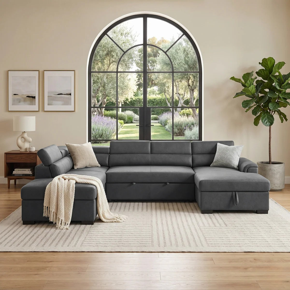 Spacious modern living room featuring the Omaha Pull-Out Sofa Bed in dark gray fabric with plush cushions, decorative pillows, a throw, and a large arched window overlooking a garden.