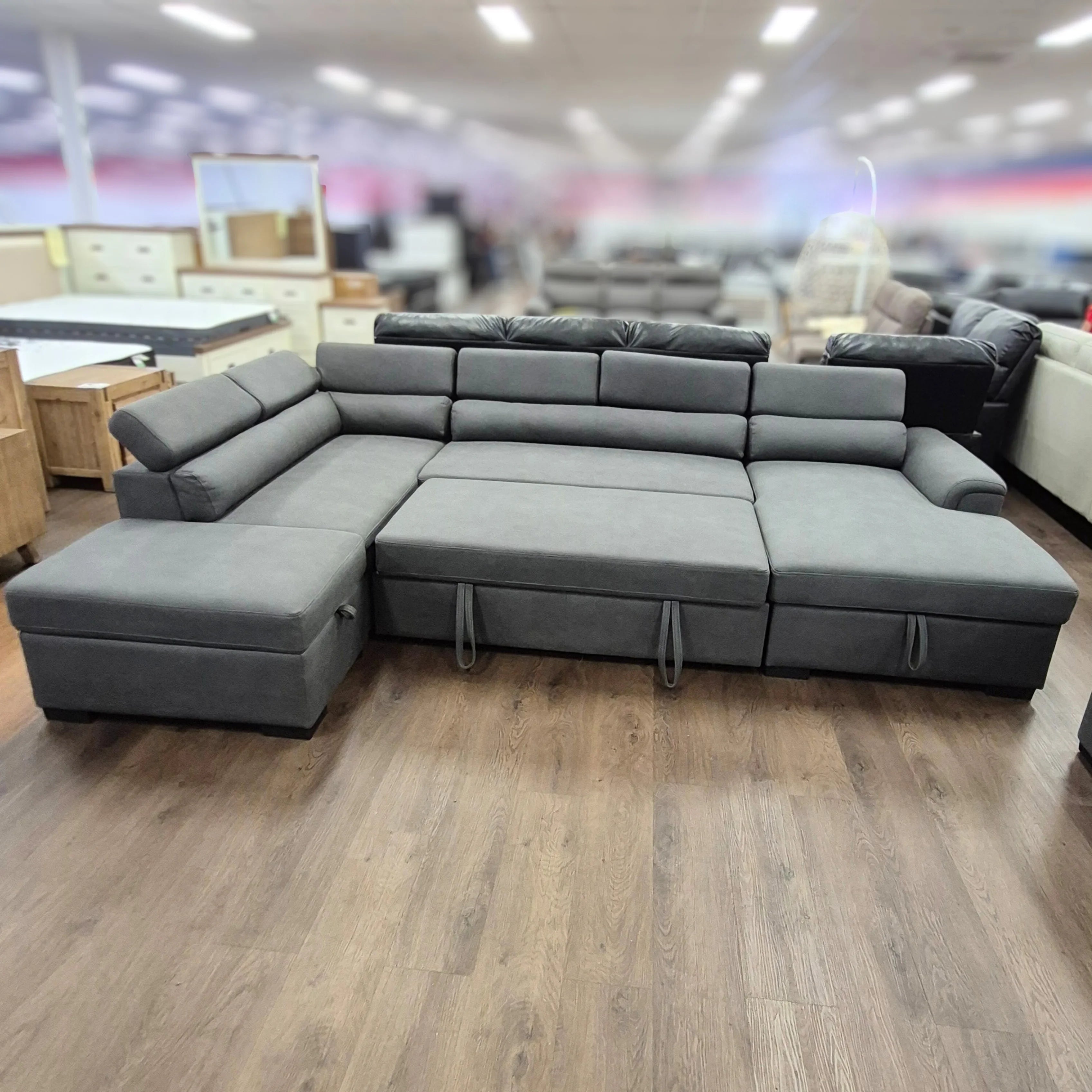 Grey pull-out sofa bed with chaise and storage in furniture showroom on wood flooring