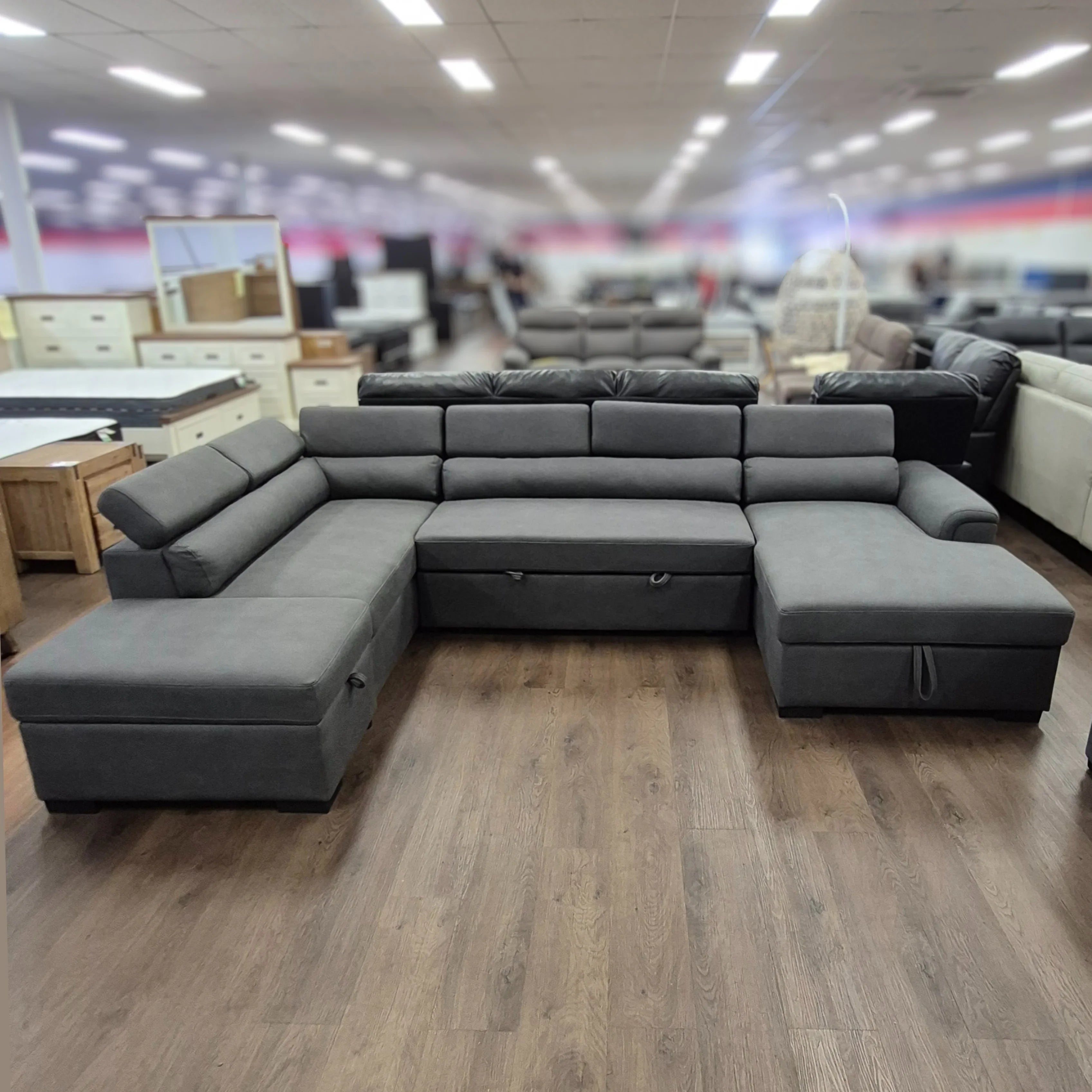 Modern grey pull-out sofa bed sectional with adjustable headrests in a furniture showroom
