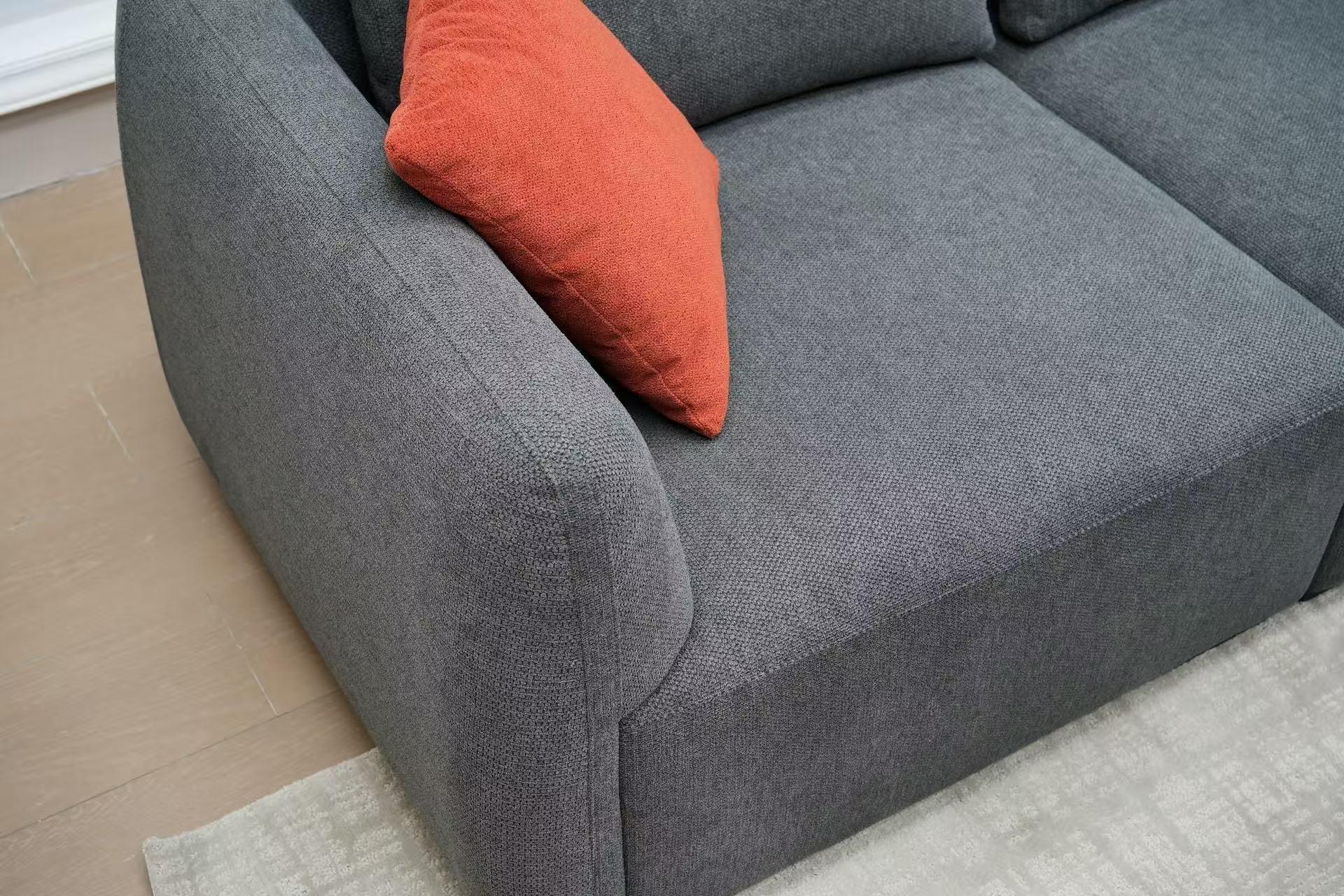 Modern grey fabric sofa with orange cushion on light rug and wooden floor