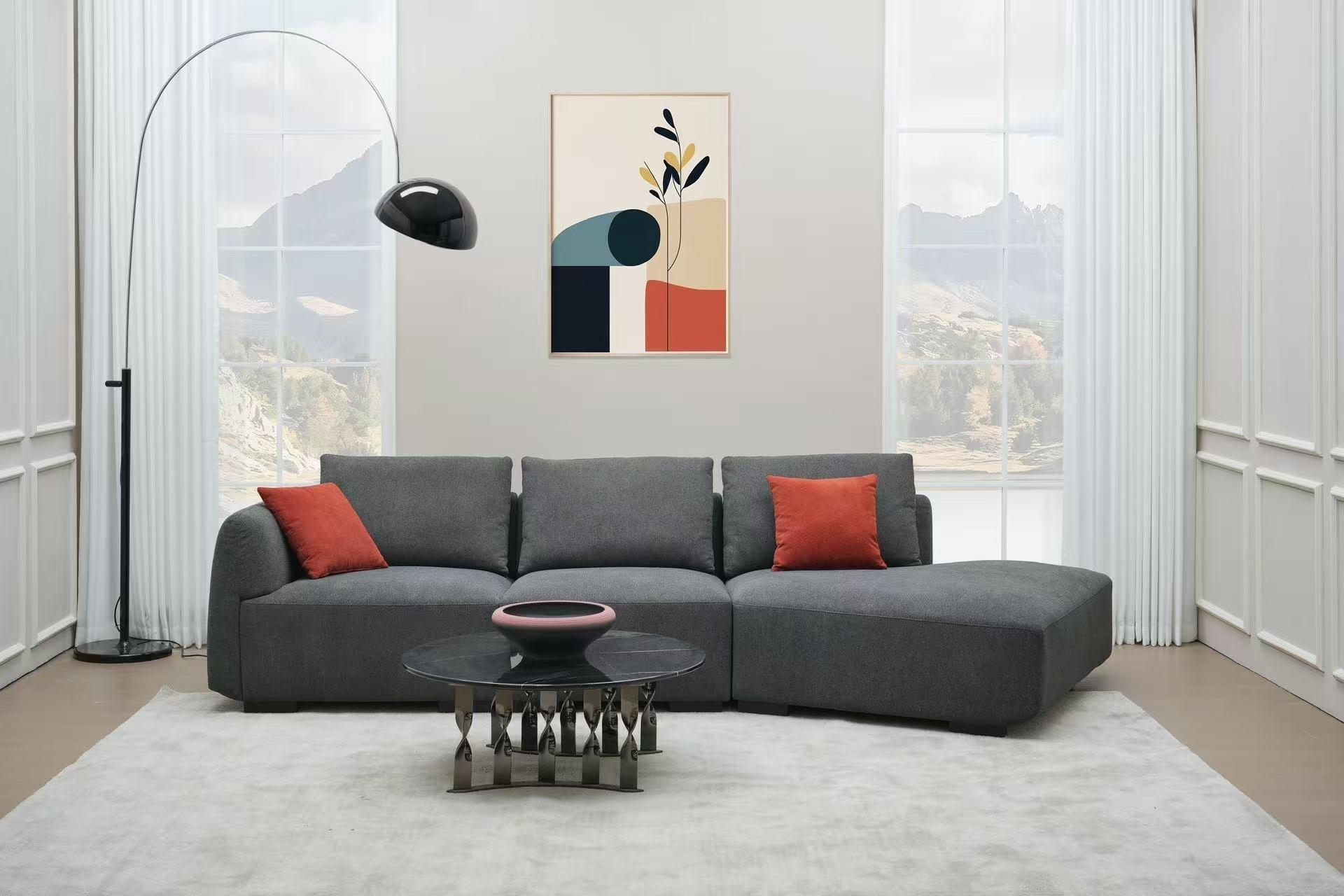 Modern grey sectional sofa with orange cushions, black coffee table, and abstract wall art in a bright living room.