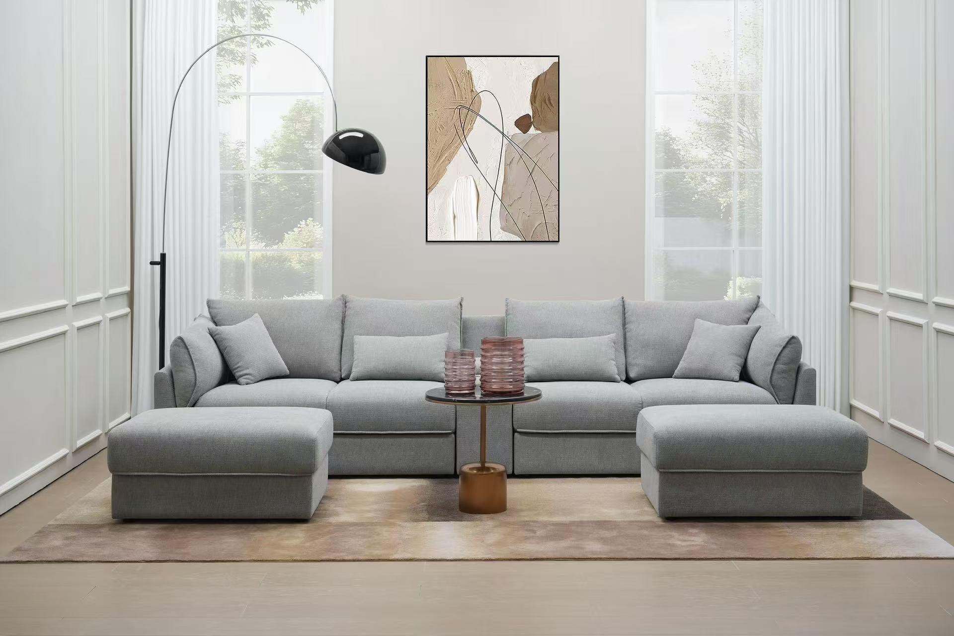 Modern living room with light grey sectional sofa, ottomans, arched floor lamp, and abstract wall art.