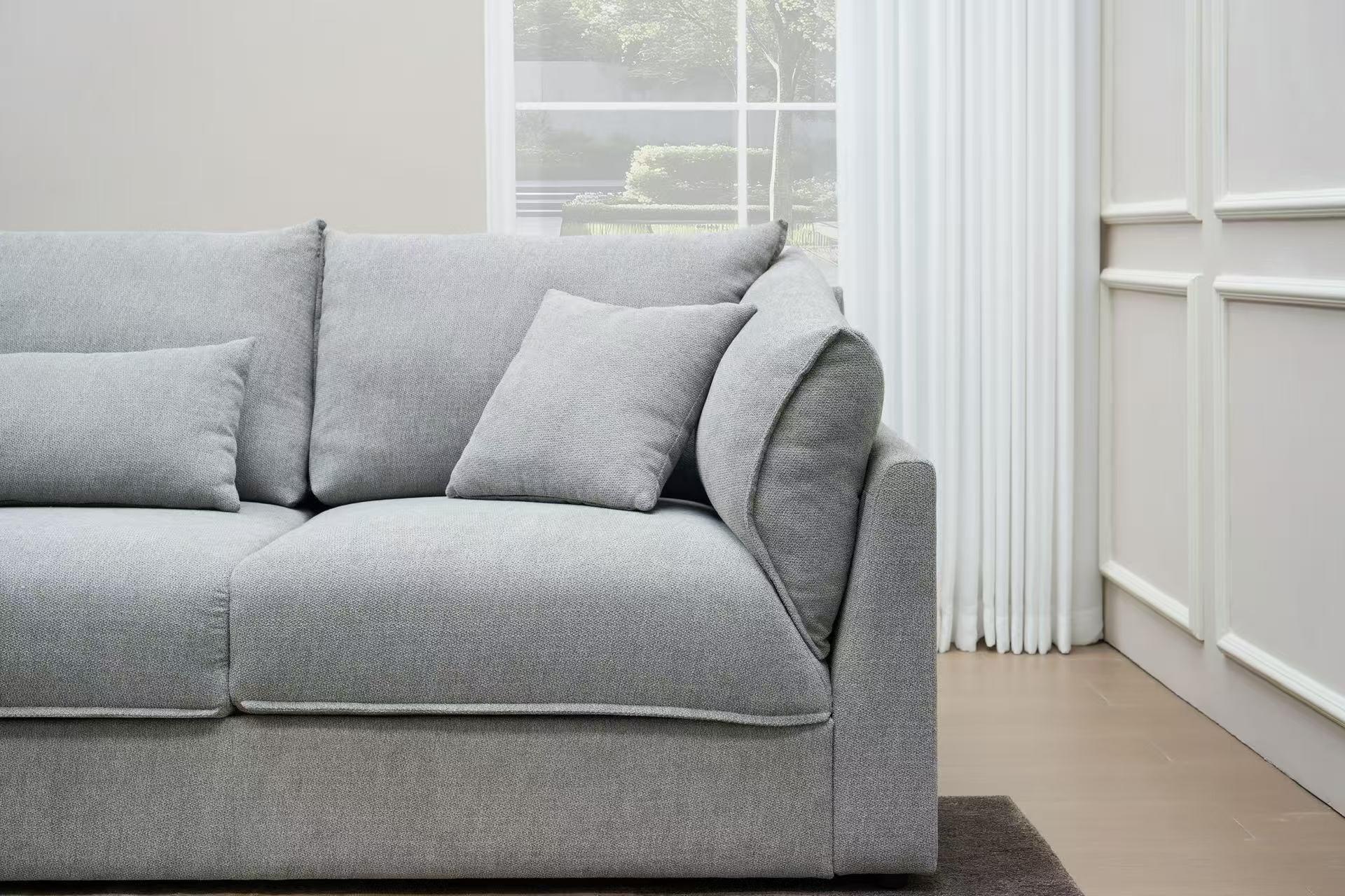 Modern light grey fabric sofa with cushions in a bright living room with window and curtains