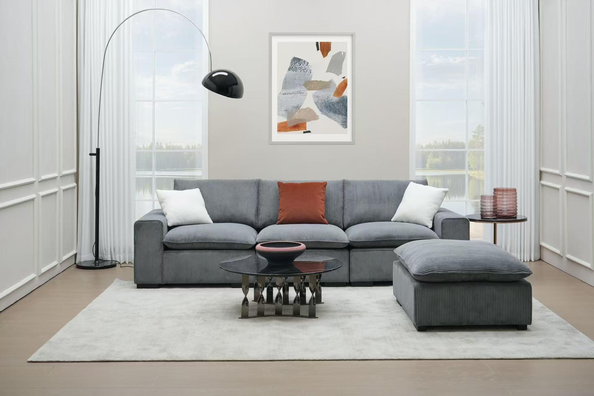 Modern grey sectional sofa set with ottoman in bright living room, glass coffee table, floor lamp, and abstract wall art