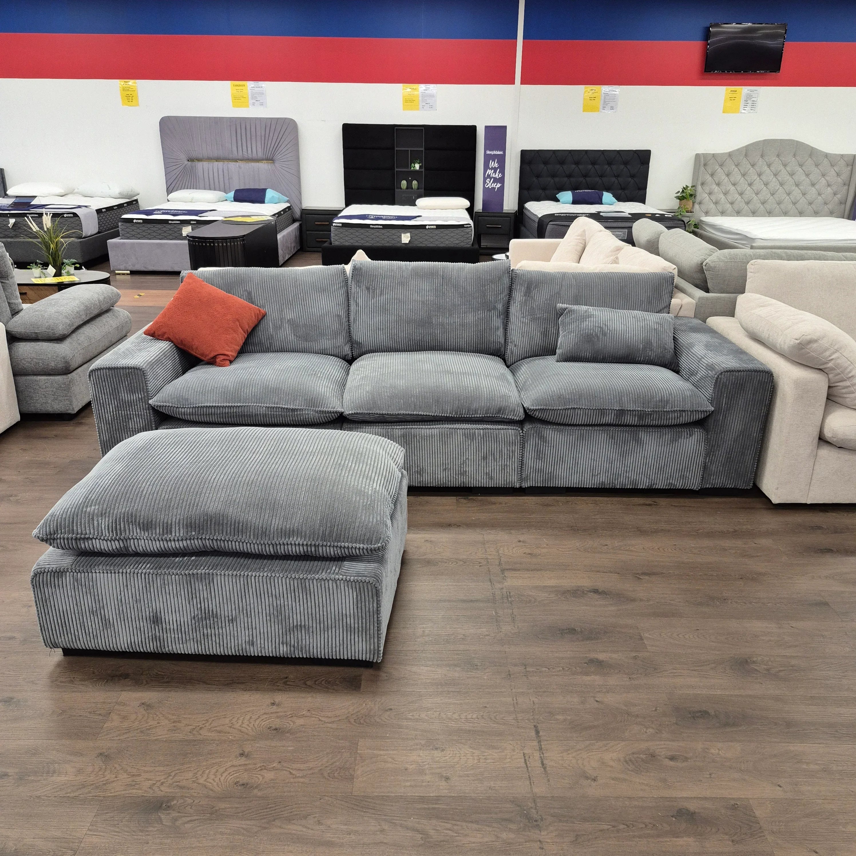 Grey corduroy sectional sofa with ottoman and orange pillow in a furniture showroom