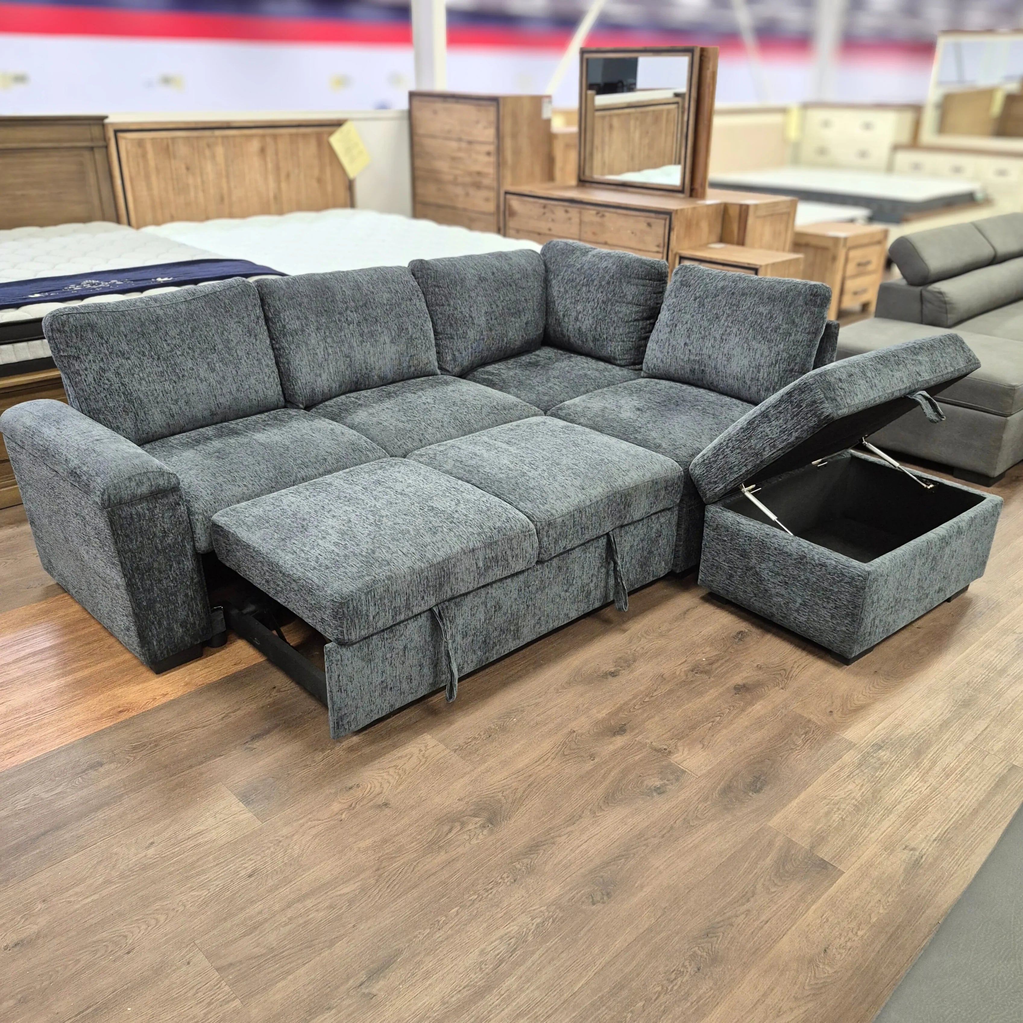 Grey fabric sofa bed with chaise lounge and open ottoman storage in a showroom