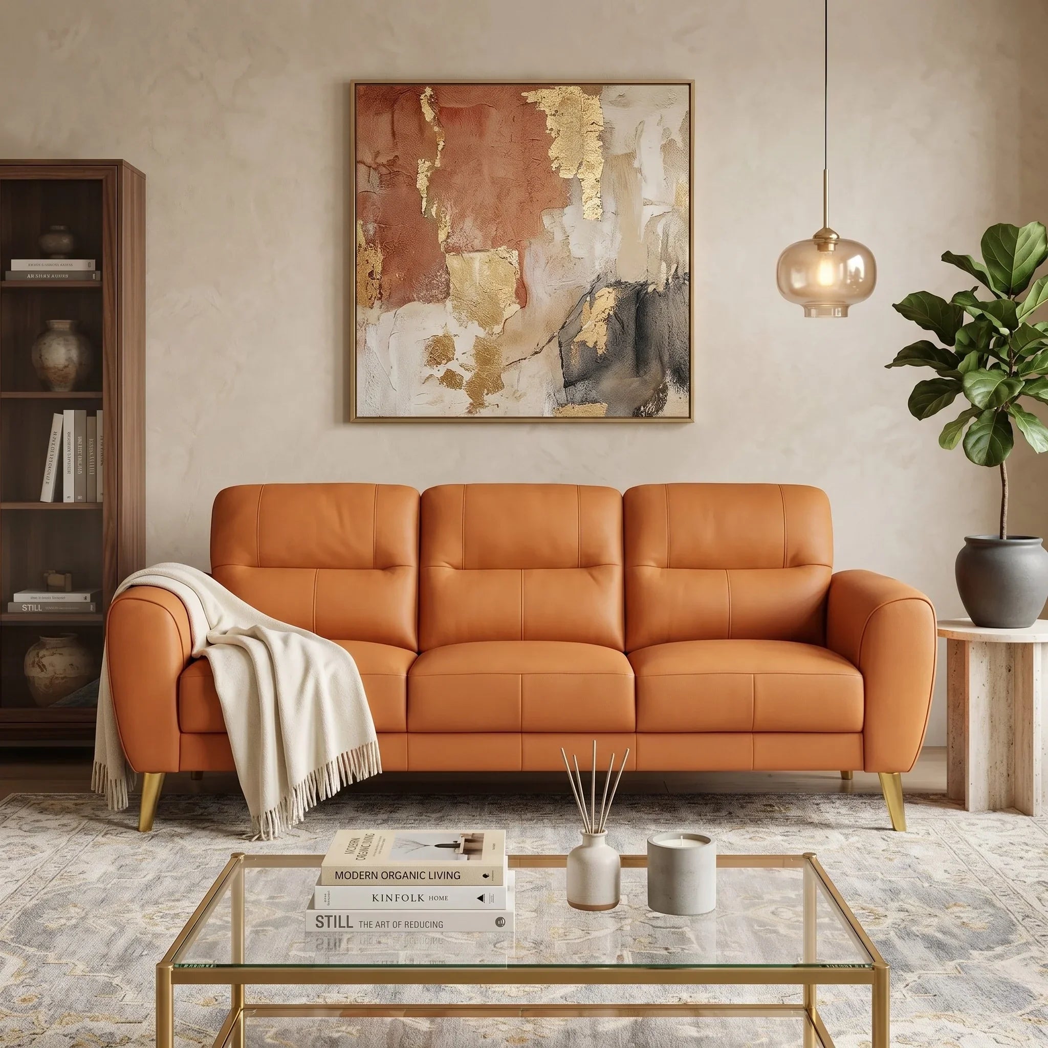 Pearl 3 Seater Leather Lounge in warm tan leather with plush cushions and gold legs, styled in a modern living room with abstract art, a glass coffee table, and soft rug.