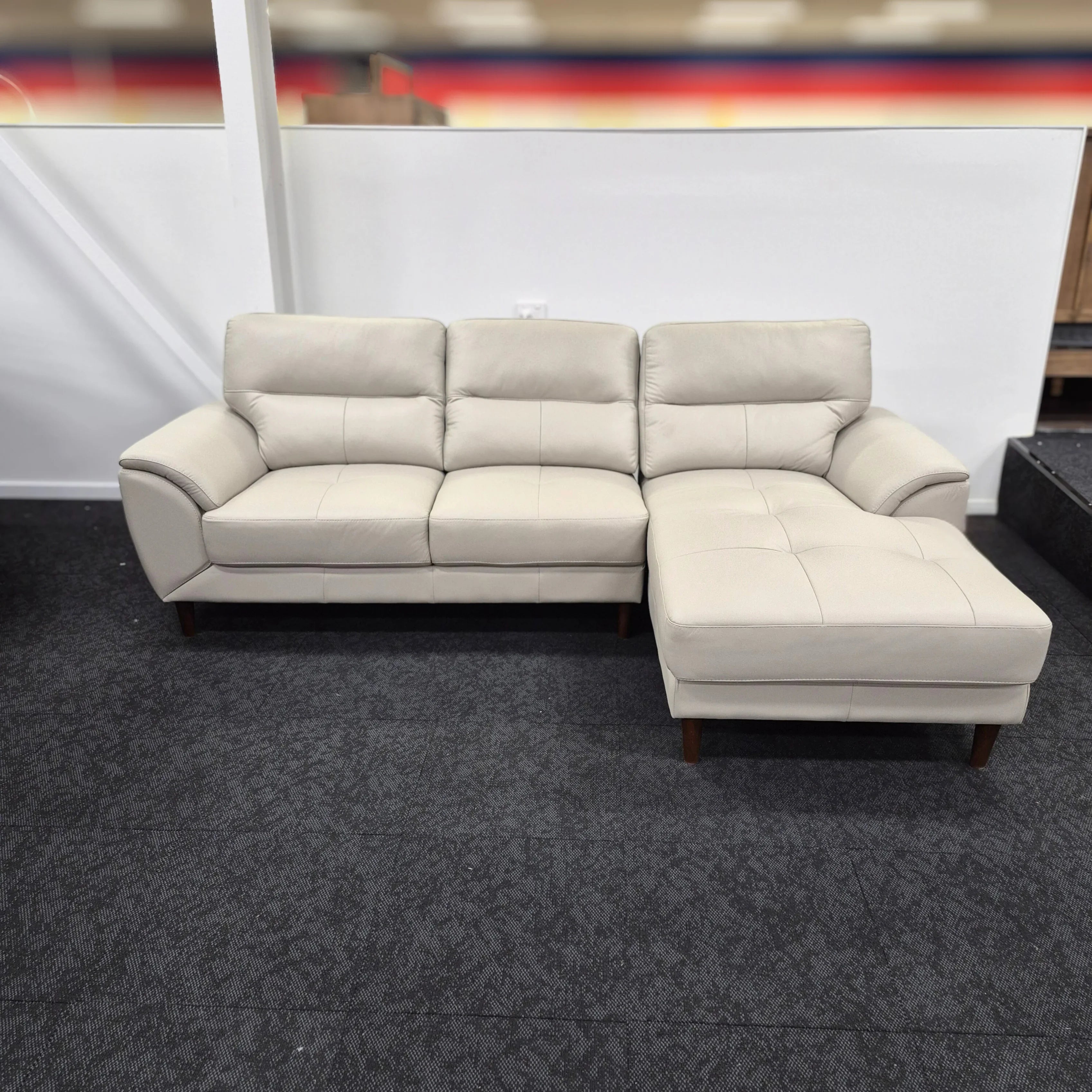 Modern light beige leather 3 seater sofa with chaise and wooden legs in showroom
